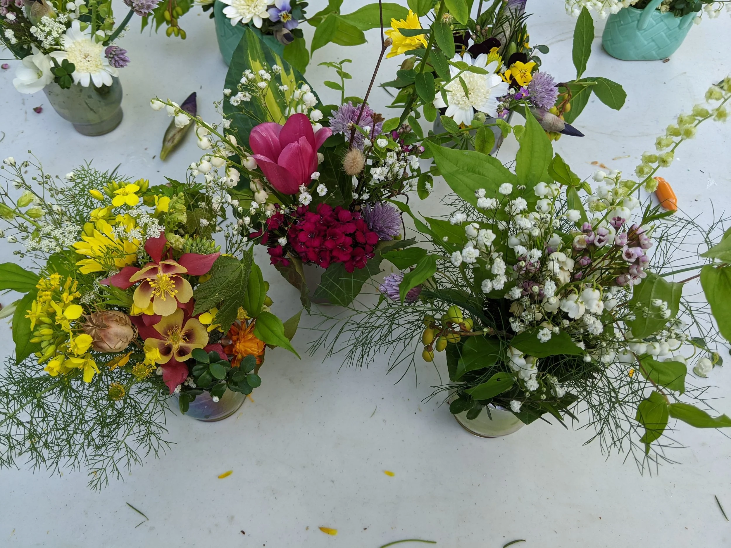 Assorted colorful flower arrangements including lilies, daisies, tulips, and baby's breath in vases on a white surface.