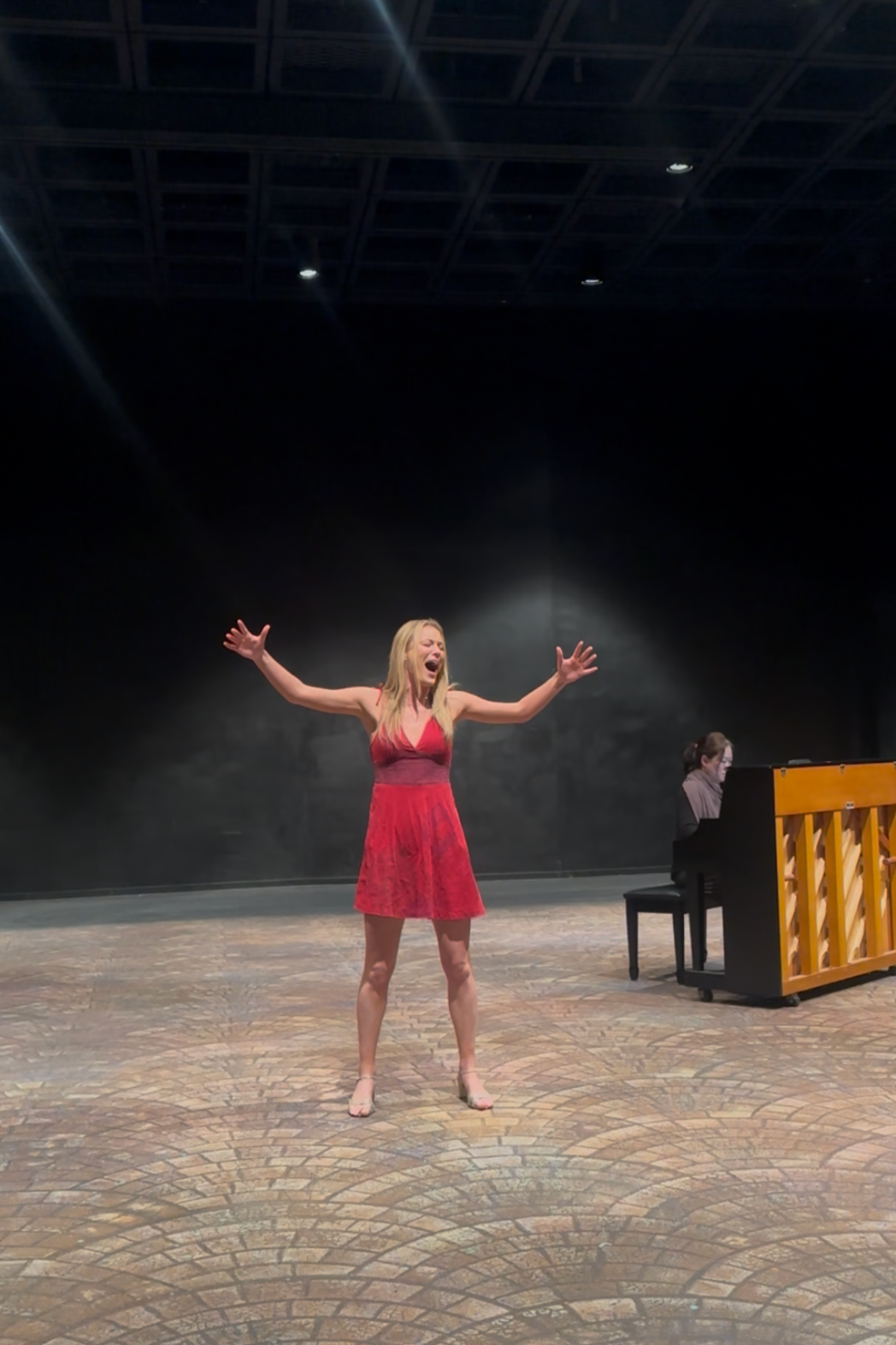 West Virginia University BFA Musical Theatre studio voice lab. A woman in a red dress singing passionately on stage with a pianist playing the piano beside her.