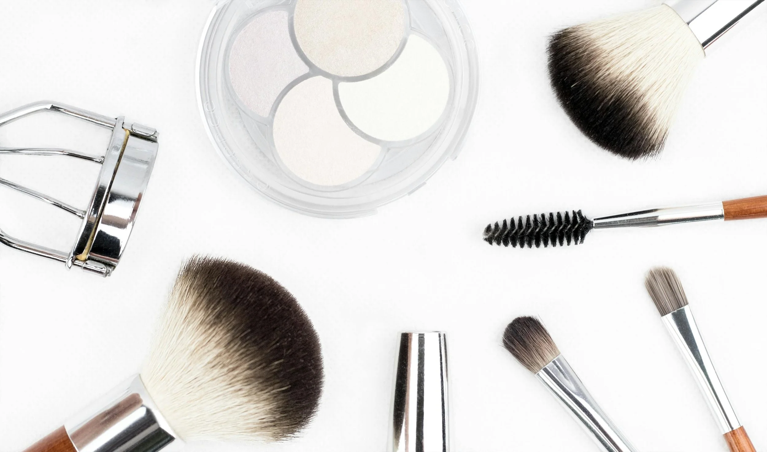 Assorted makeup brushes, eyelash separator, and cosmetic palette on a white background.