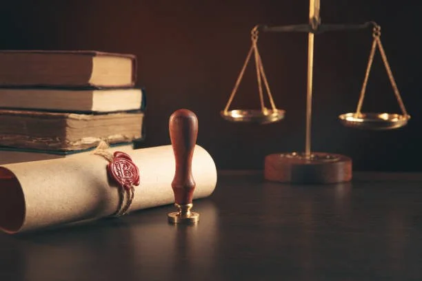A set of old books, a sealed document with a wax stamp, and a brass balance scale on a dark wooden surface.
