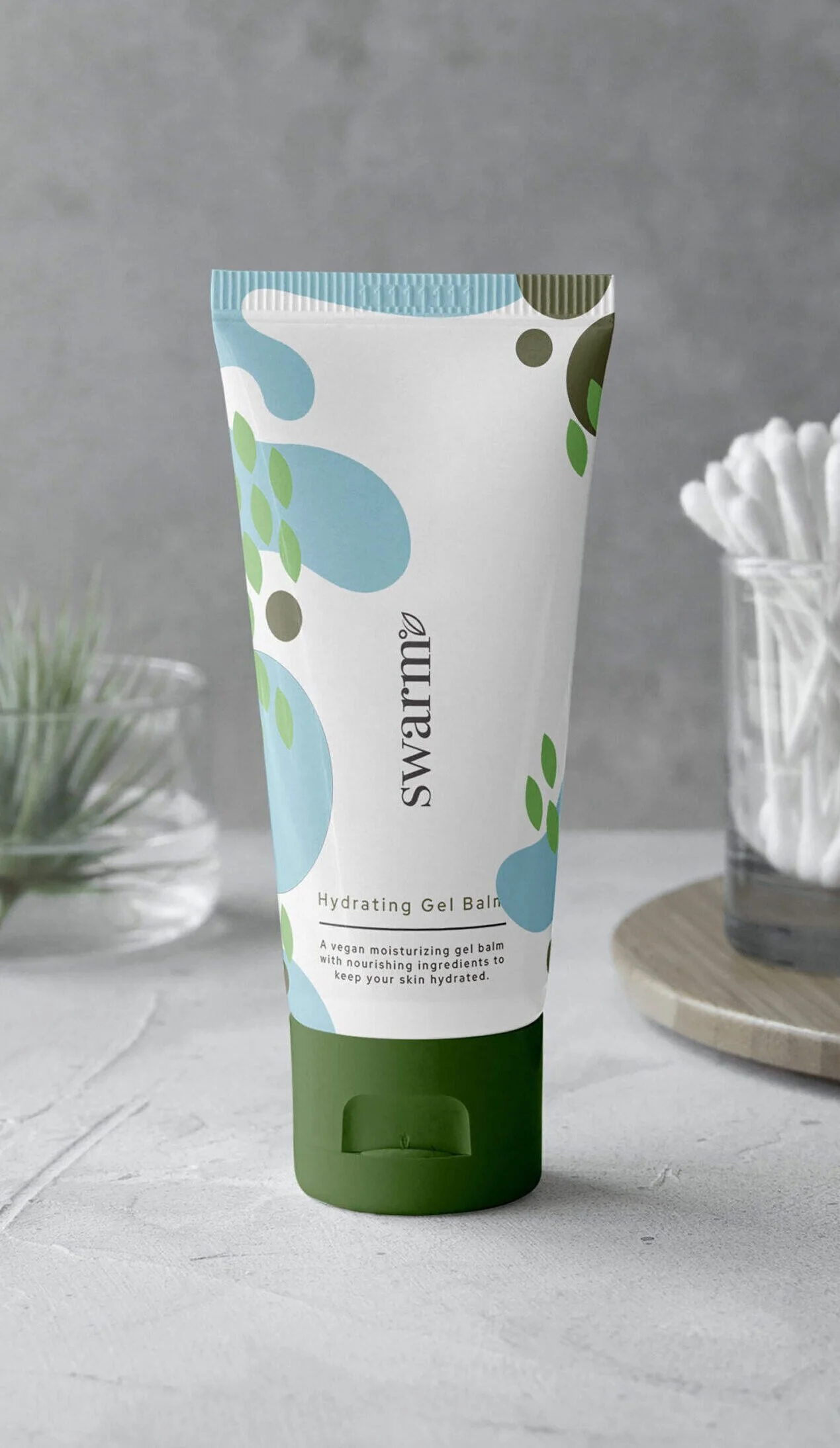 A tube of Swarm hydrating gel balm on a white surface with a gray background, flanked by a small potted plant and a glass container of cotton swabs.