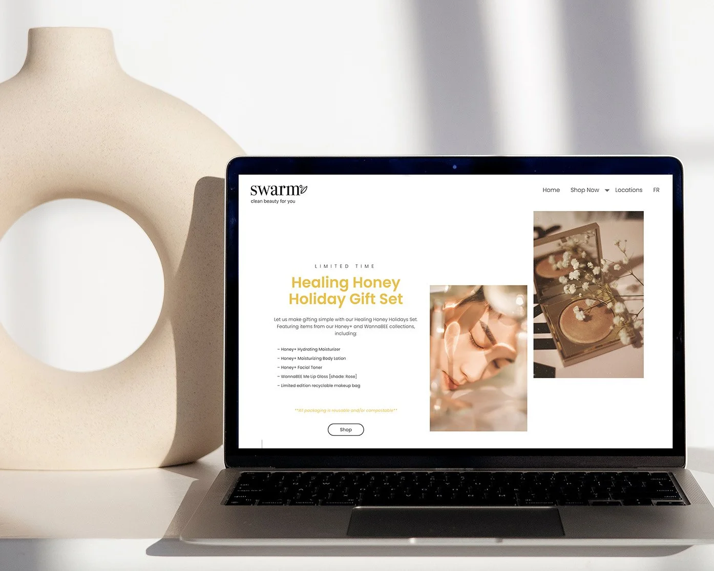 Laptop displaying a skincare product website on a white table next to a modern beige vase with a large circular cutout.