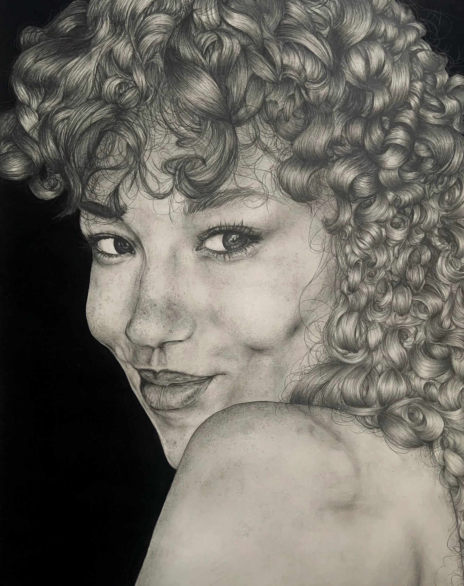 A detailed pencil sketch of a woman with curly hair in black and white. She is smiling subtly, with one eye looking directly at the viewer and her shoulder slightly turned.