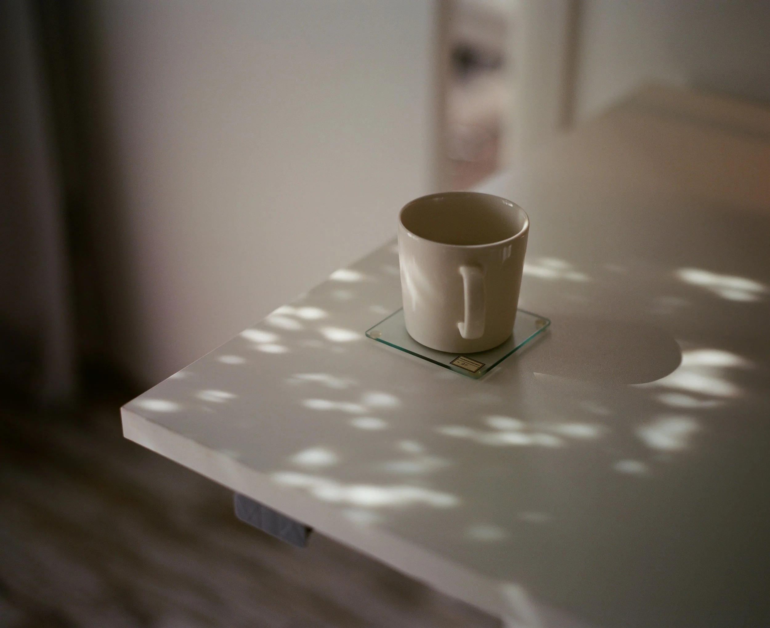 A white ceramic mug on a glass coaster on a white bench.