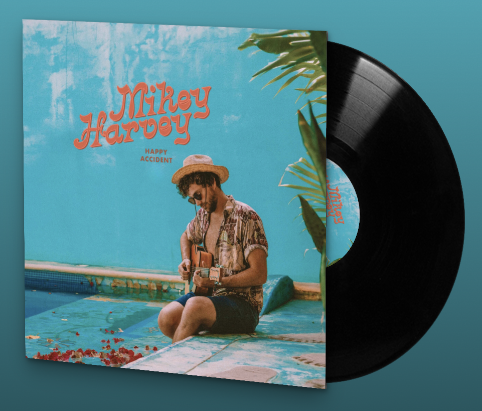 Vinyl record album cover titled "Mikey Harvey Happy Accident" featuring a man sitting by a pool playing guitar, wearing a straw hat, sunglasses, and a patterned shirt, with a light blue sky and some palm leaves in the background.