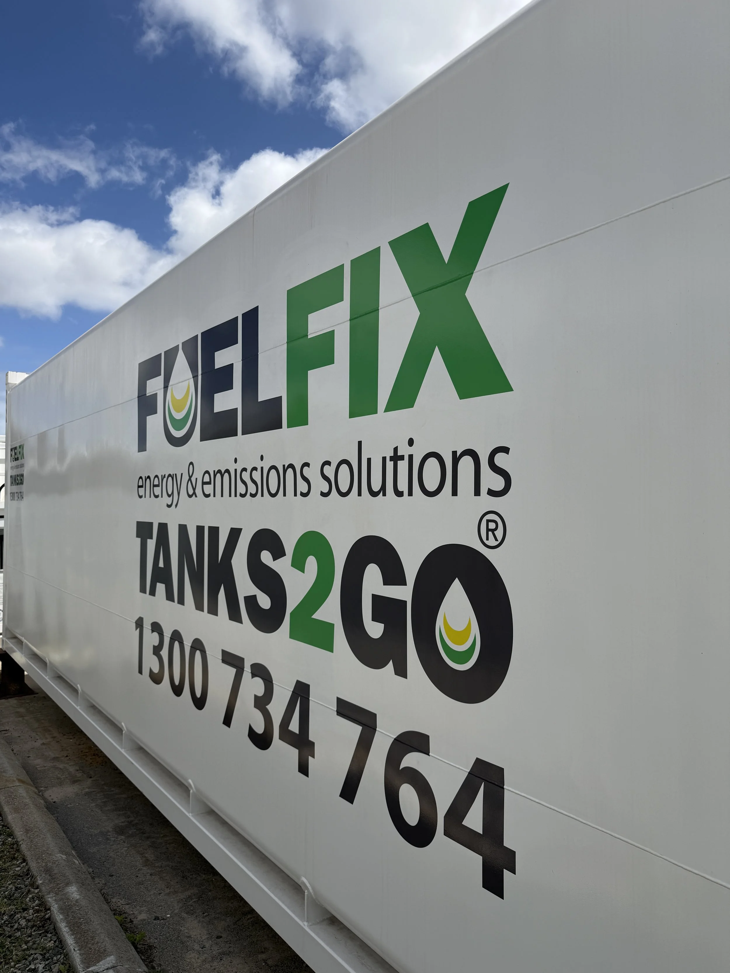 White fuel tank side with green and grey text and logo for Fuel Fix and emissions solutions, displaying contact phone number.