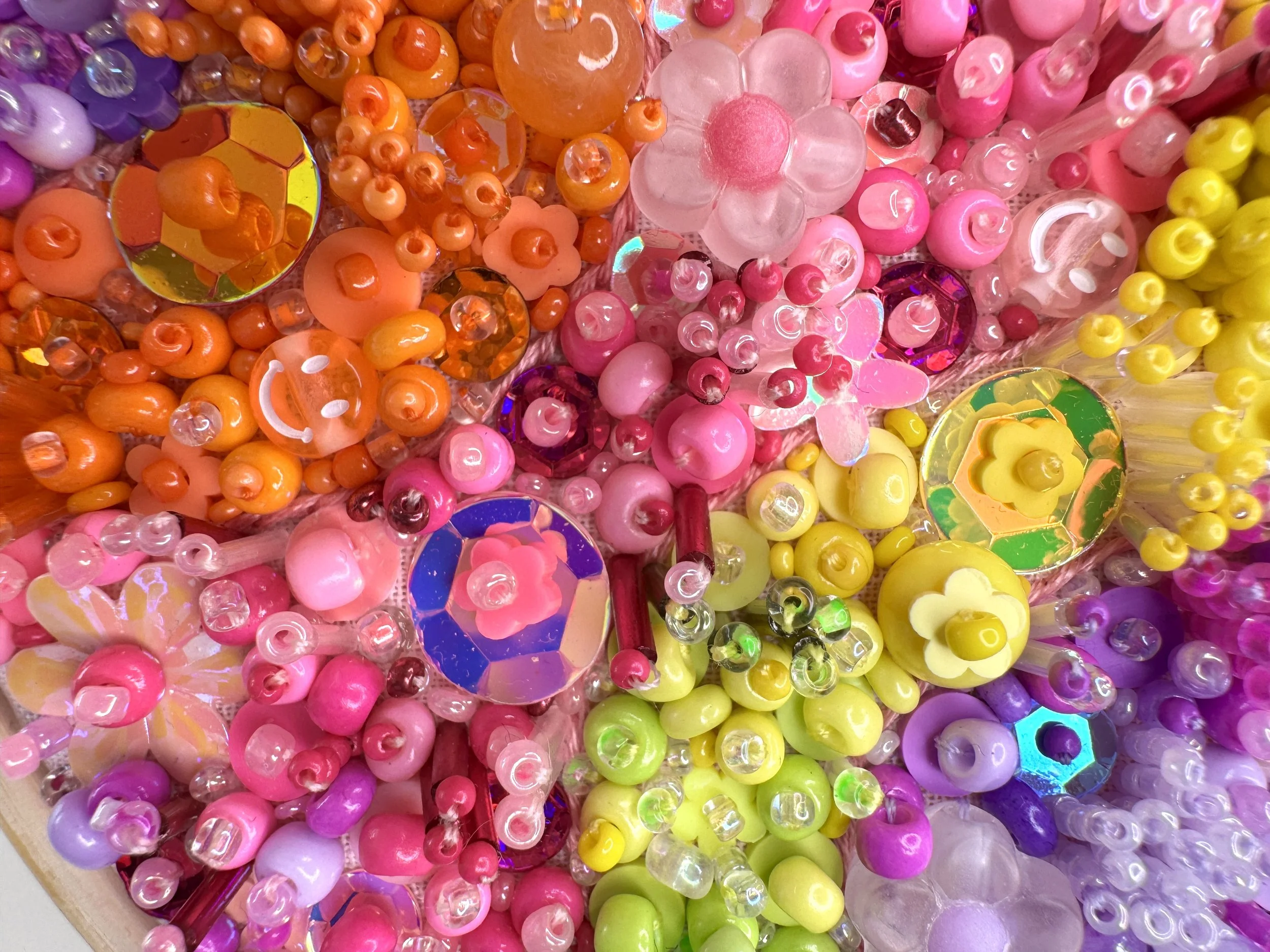 Close-up of a collection of colorful plastic beads and sequins in shades of pink, orange, yellow, purple, and green.