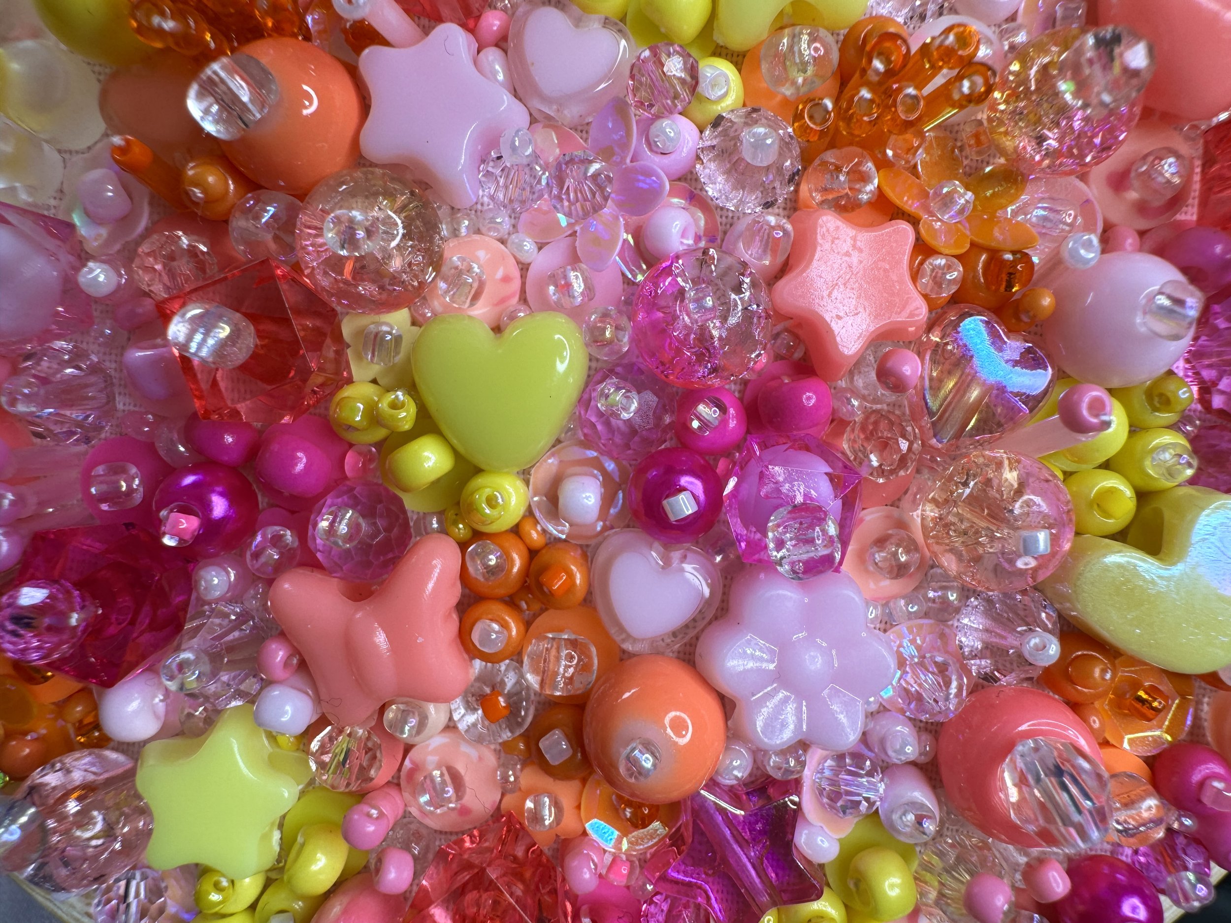 A close-up of colorful plastic beads and charms, including pink hearts, yellow hearts, orange beads, and clear faceted beads.
