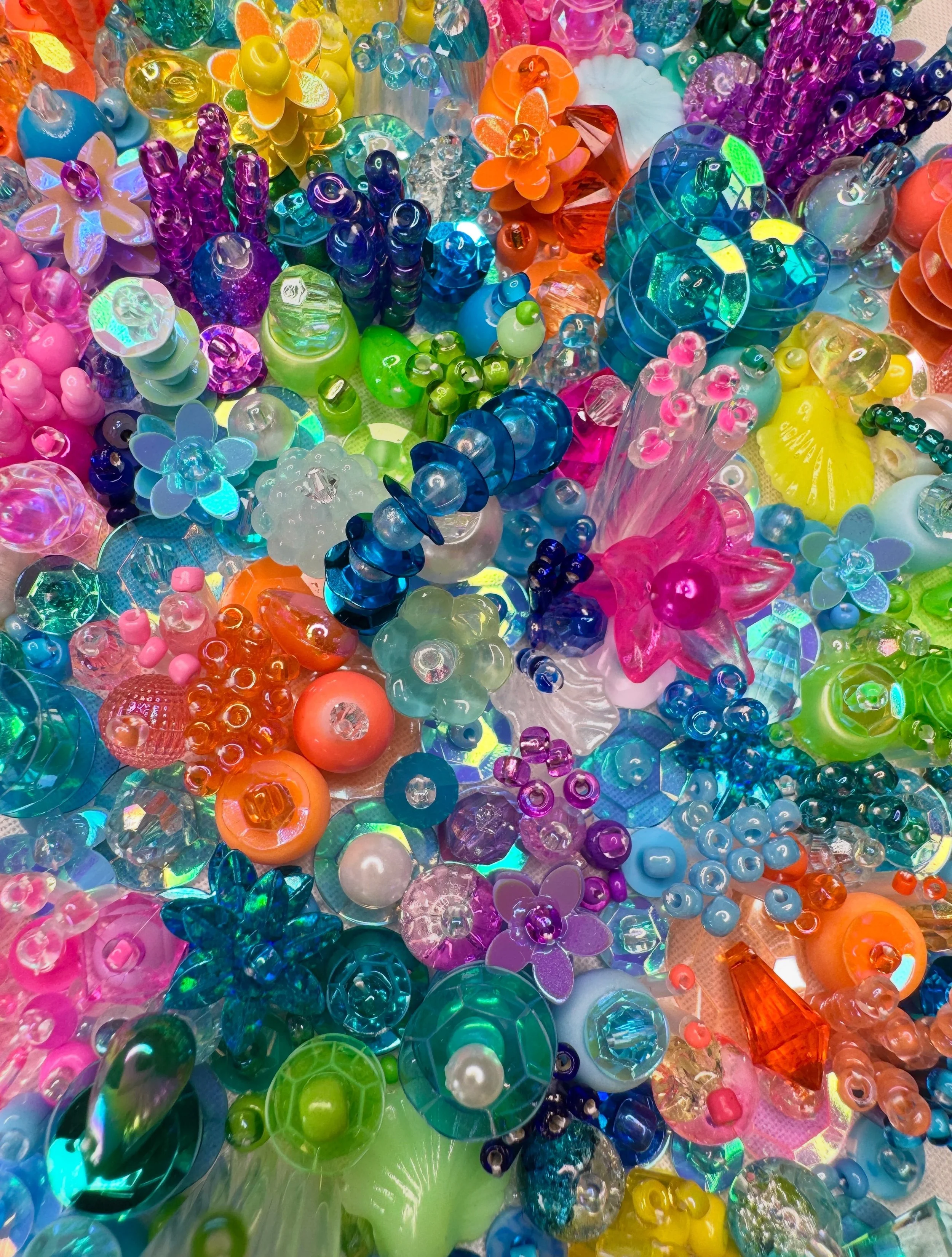 Colorful assortment of glass and plastic beads, flowers, and decorative objects arranged closely together in a coral inspired pattern.