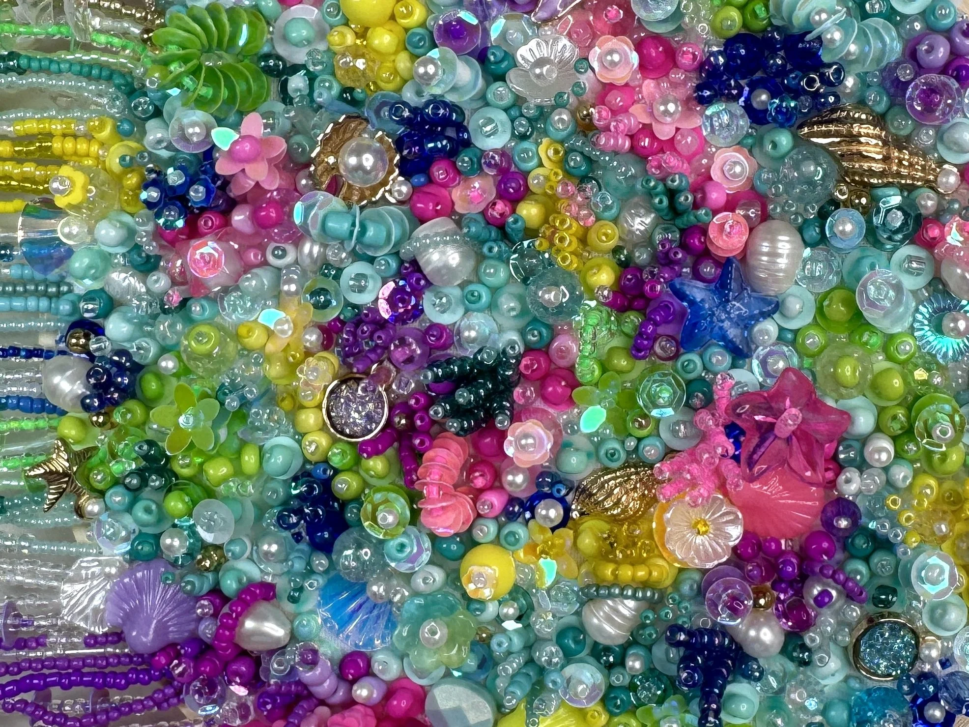 A collection of colorful, shiny plastic beads and decorative elements, including pearls, flowers, and shells, in various bright shades of pink, blue, green, yellow, and purple.