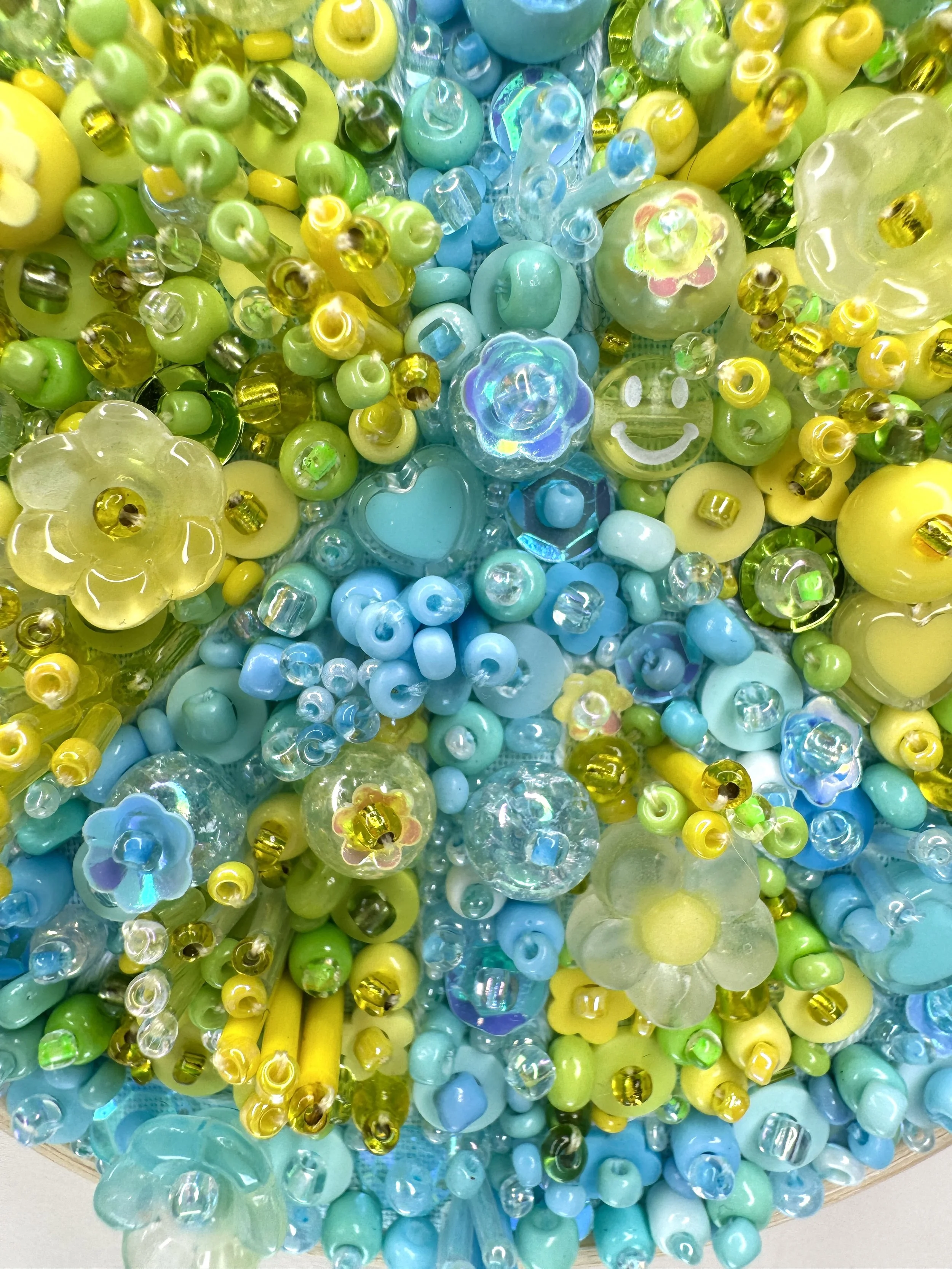Close-up image of a colorful glass art installation with various yellow, green, and blue glass beads, flowers, and decorative shapes.