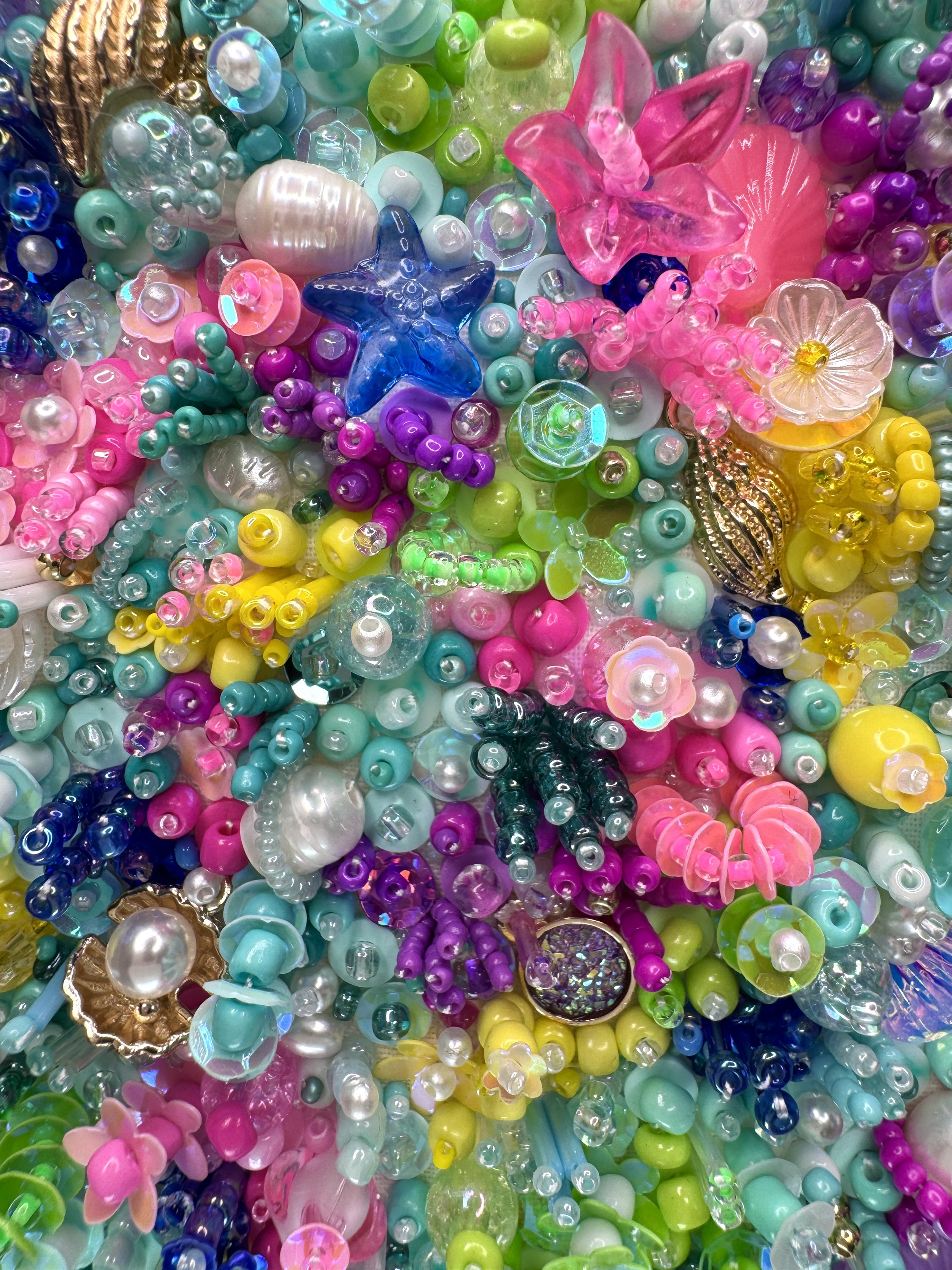 Close-up of hand embroidered colourful beads, including pink flowers, star-shaped beads, round beads, and metallic accents.