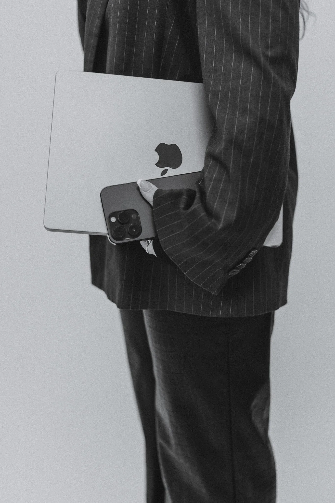 Henkilö kannattelee MacBook-laptopia ja iPhonea, kädessään. Tausta on harmaa.