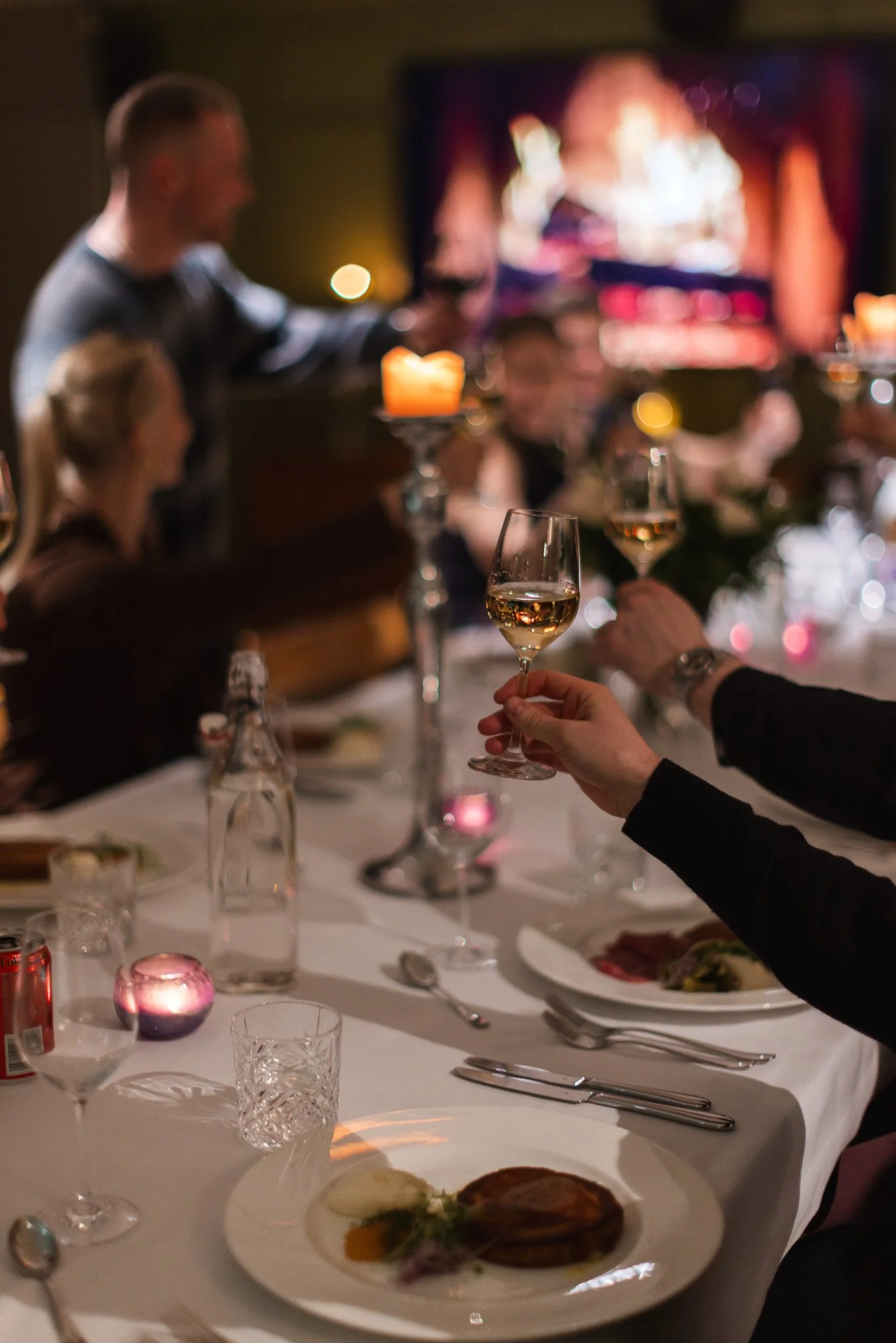 Juhlapöytä, jossa on laseja viiniä, ruokaa ja kynttilöitä, illallisella.
