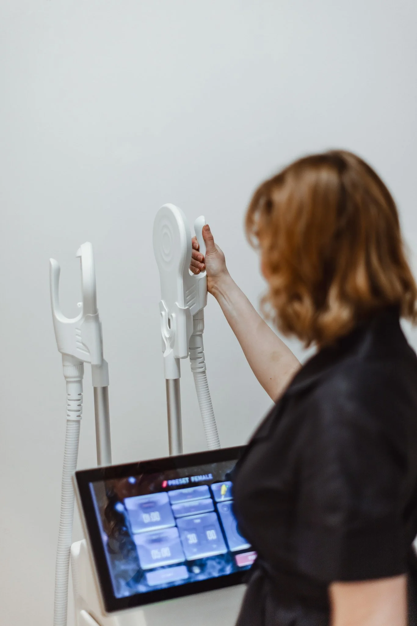 Nainen katsoo ja käyttää lääketieteellistä laitetta, jonka vieressä on muita laitteita, valkoisella taustalla.