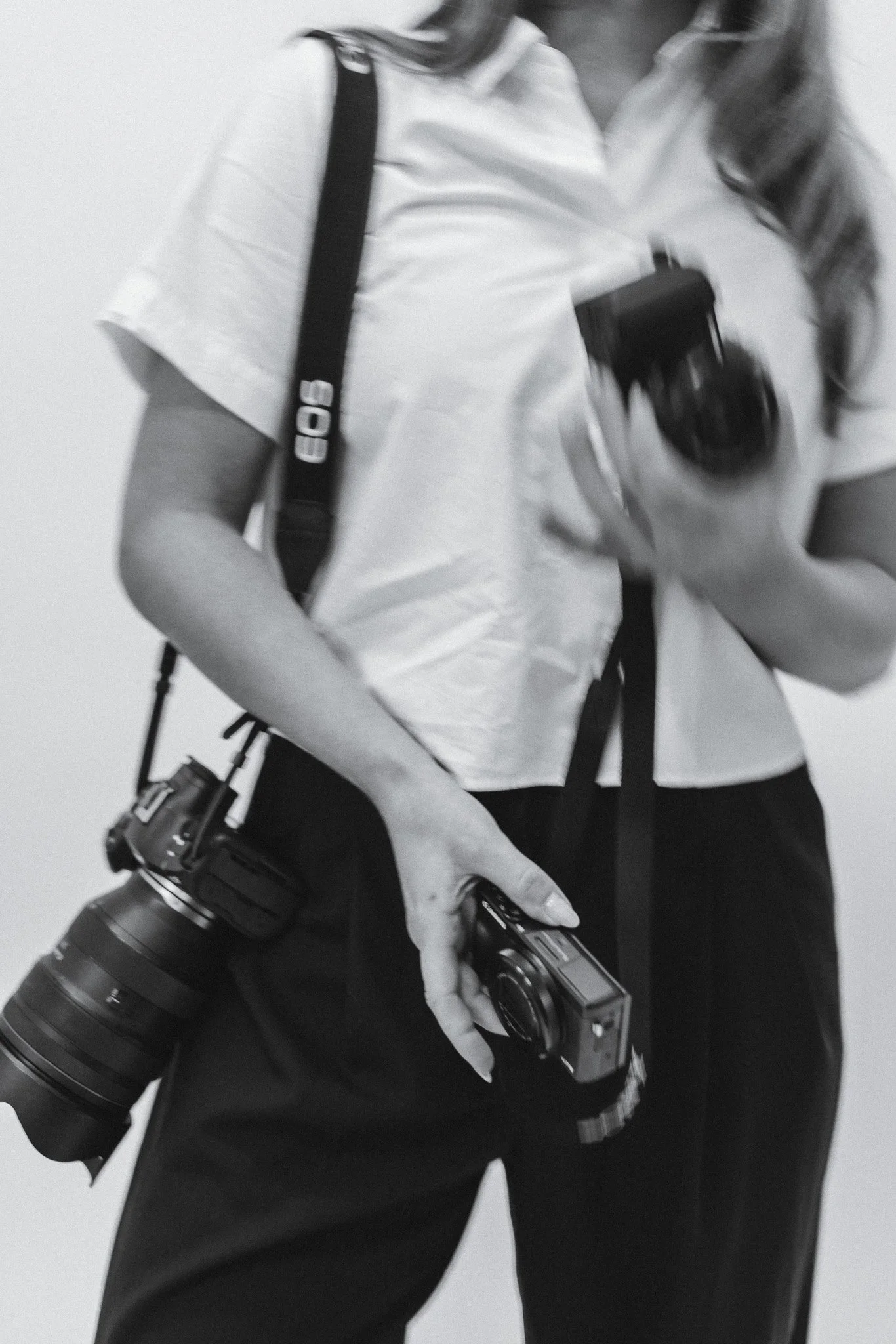 Kuva henkilöstä, jolla on kamera ja kamerajalusta, sekä kameroita ja objektiiveja, varusteet kädessä.