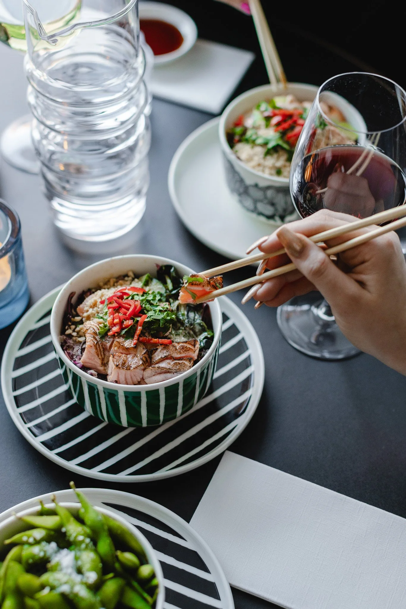 Lautasella ja kulhossa sushia, lasi punaviiniä, vettä ja soijakastiketta, alustan ja pienen kynttilän.