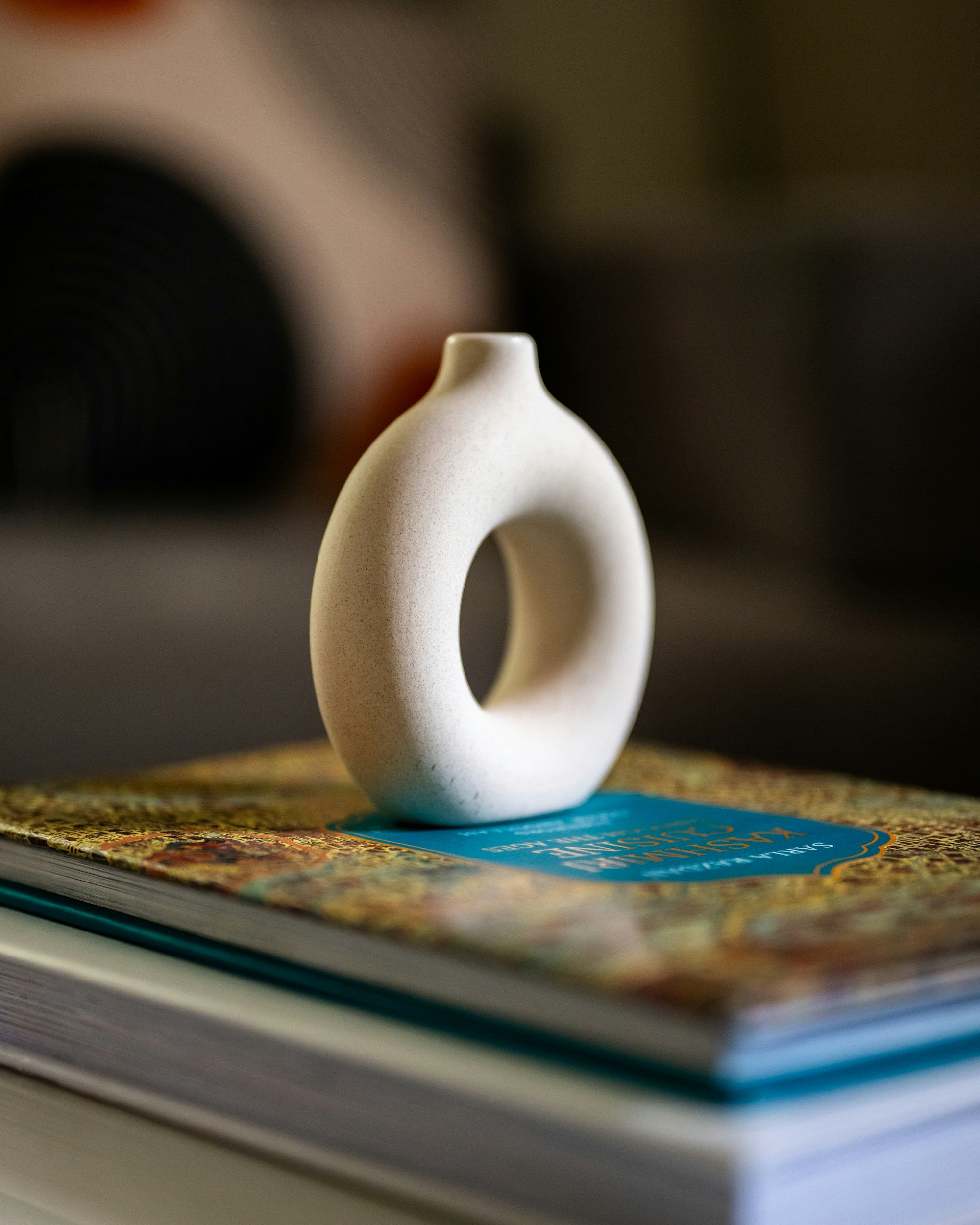 A beige ceramic or stone sculpture with a circular hole in the center, placed on top of colorful magazines or books on a table.
