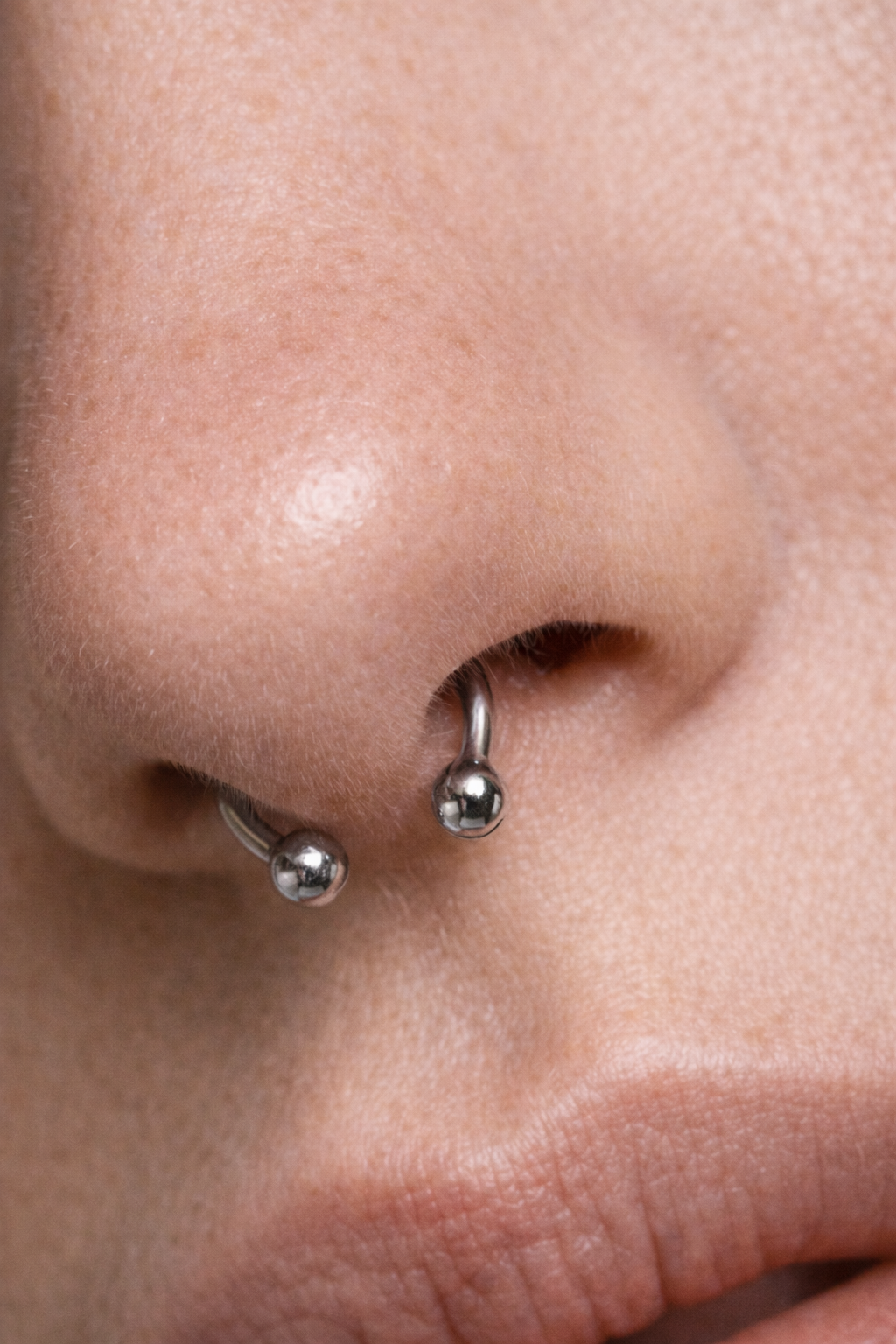 Close-up of a person's nose with a septum piercing featuring two silver ball rings. AI influencer, AI persona, AI design, custom AI.