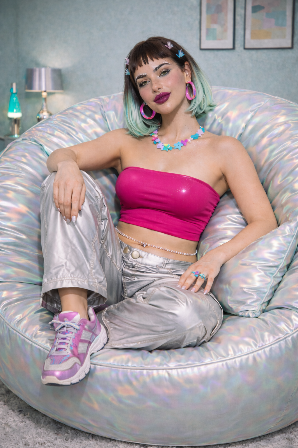 Y2K woman with teal and brown hair sitting on a shiny, iridescent, circular chair in a room with pastel-colored wall art, wearing a pink strapless top, metallic pants, pink sneakers, and colorful jewelry. Custom AI model, AI influencer.