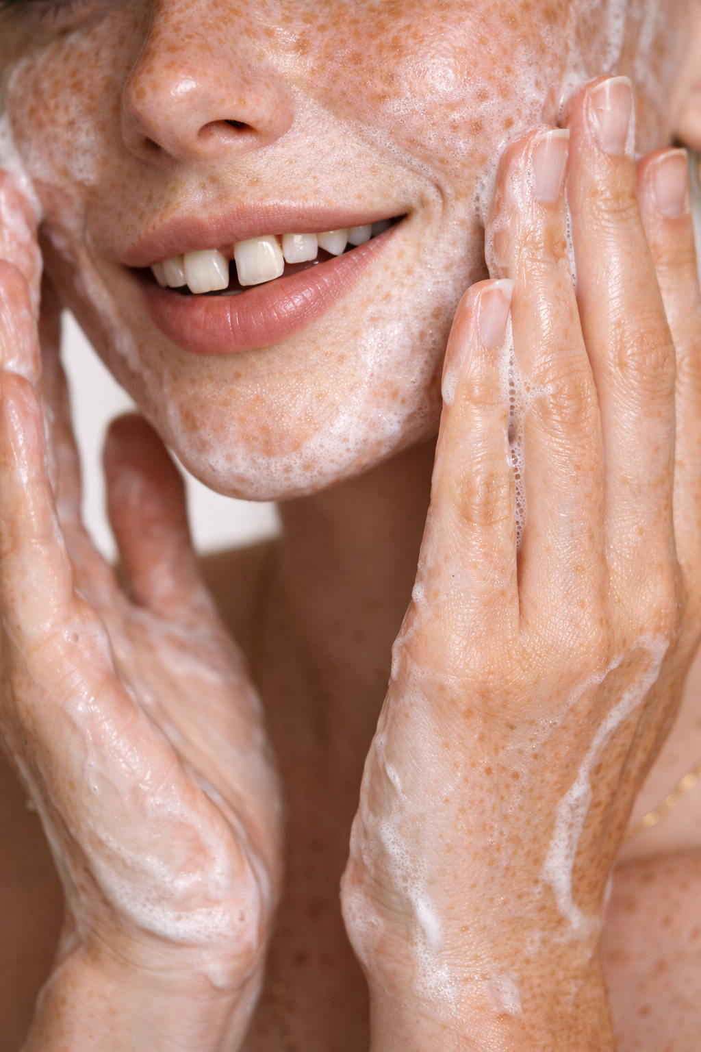 Close-up of a woman washing her face with soap, soap bubbles on her skin, smiling slightly. Custom AI influencer, custom AI content creator.