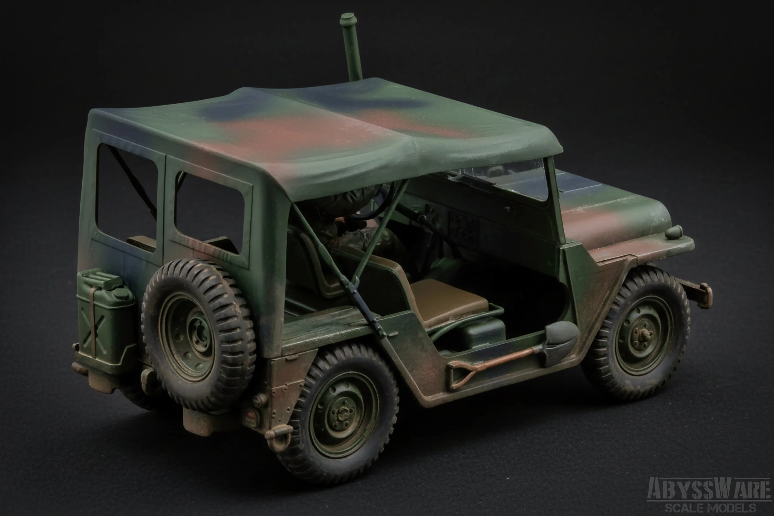 Scale model of a military green, vintage off-road vehicle with a spare tire on the back and a jerry can attached on the rear left side, set against a black background.