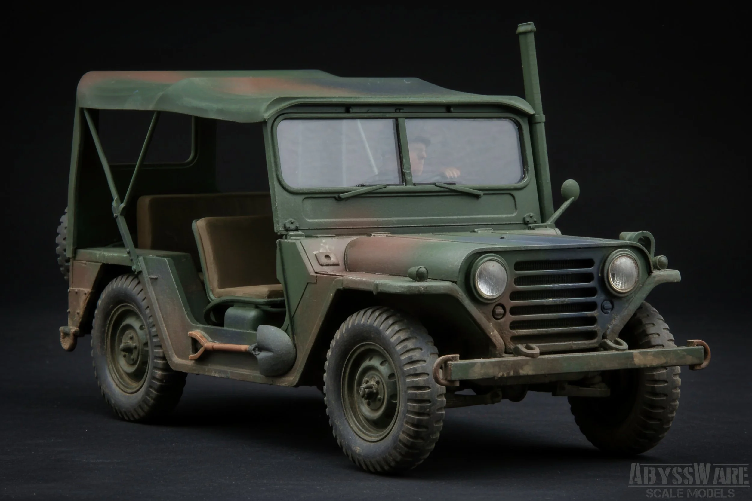 Scale model of a military jeep with green camouflage paint, beige seats, and detailed rugged tires against a black background.