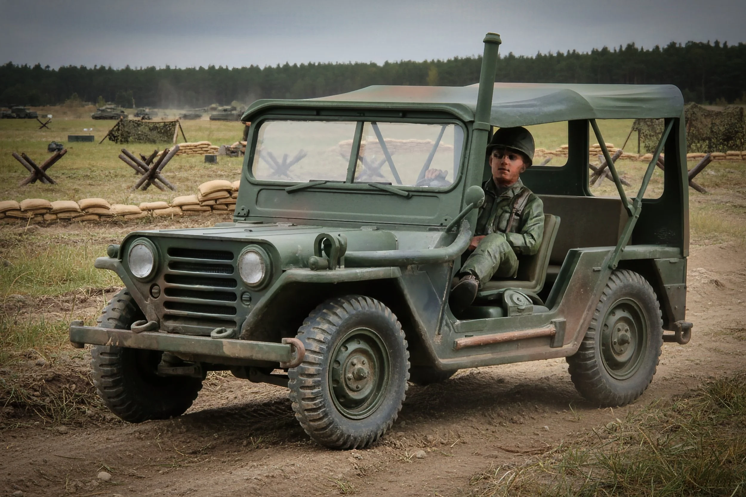 A young soldier in military attire driving a vintage green military jeep through a battlefield with sandbags and barbed wire in the background.