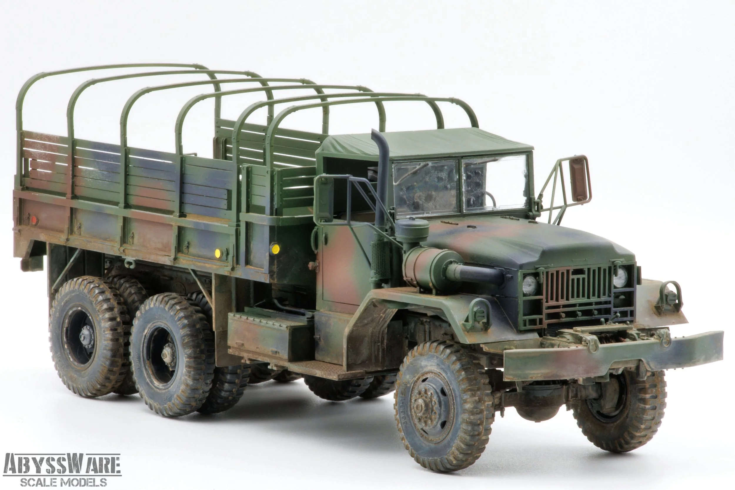 Model military cargo truck with six wheels, camouflage paint, and an open flatbed with side rails, on a white background.