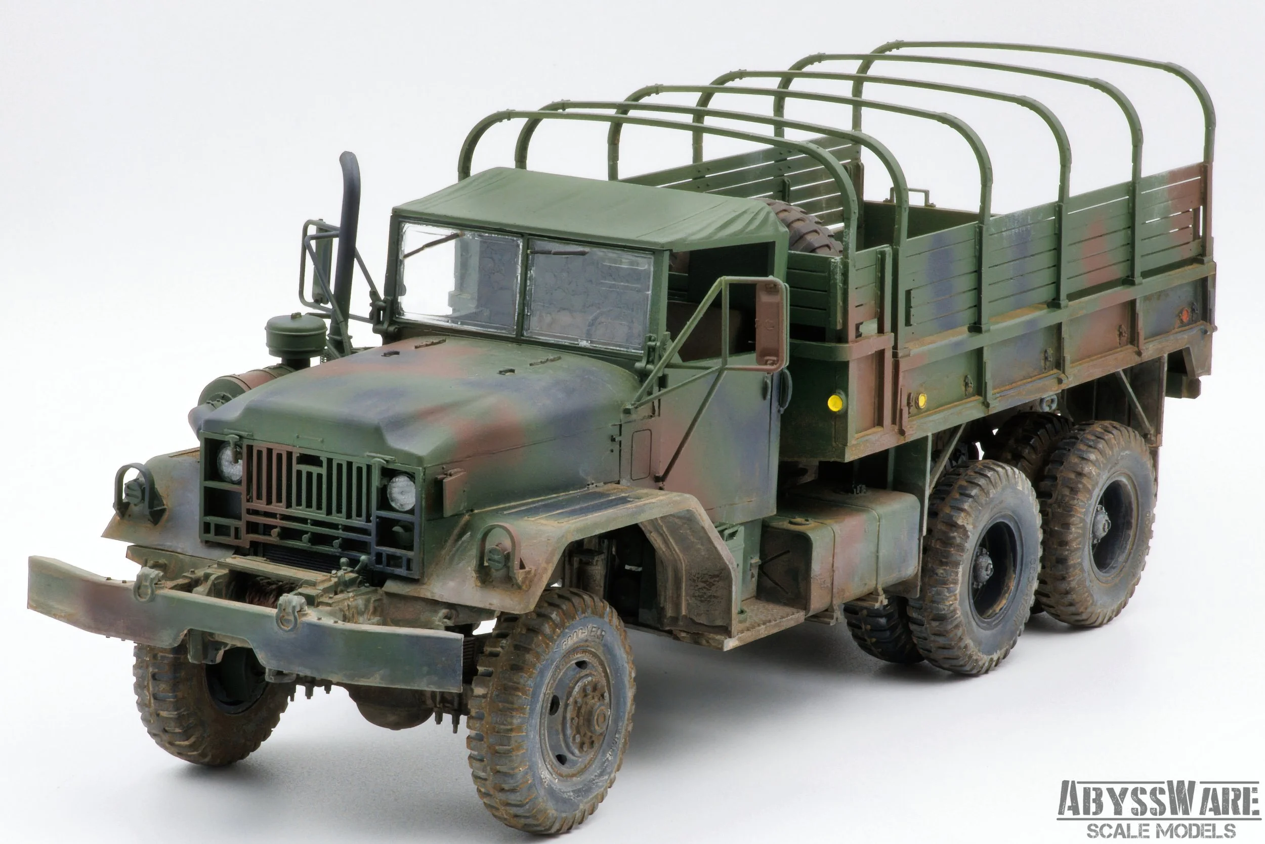 Model of a military cargo truck with a camouflage paint job, six large tires, and a flatbed cargo area with a curved metal frame.