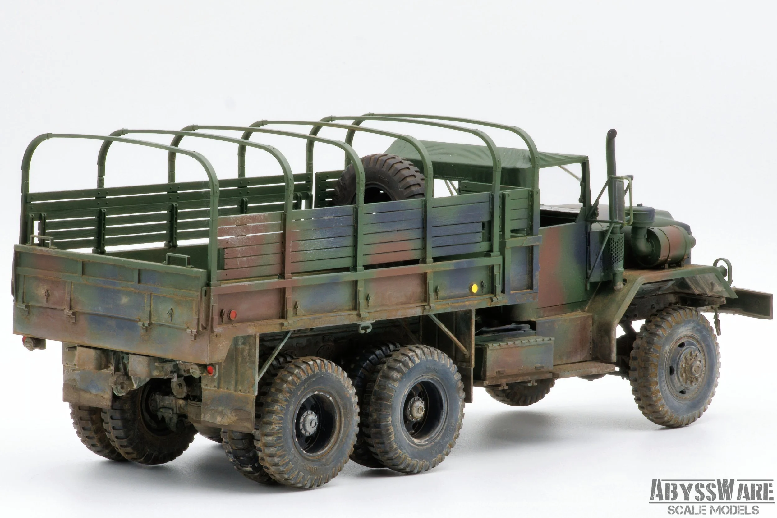 Model of a military truck with a camouflage paint job, featuring six wheels, a flatbed with side rails, and a spare tire mounted on the bed. The truck is displayed on a plain white background with a logo from AbyssWare Scale Models in the bottom righ