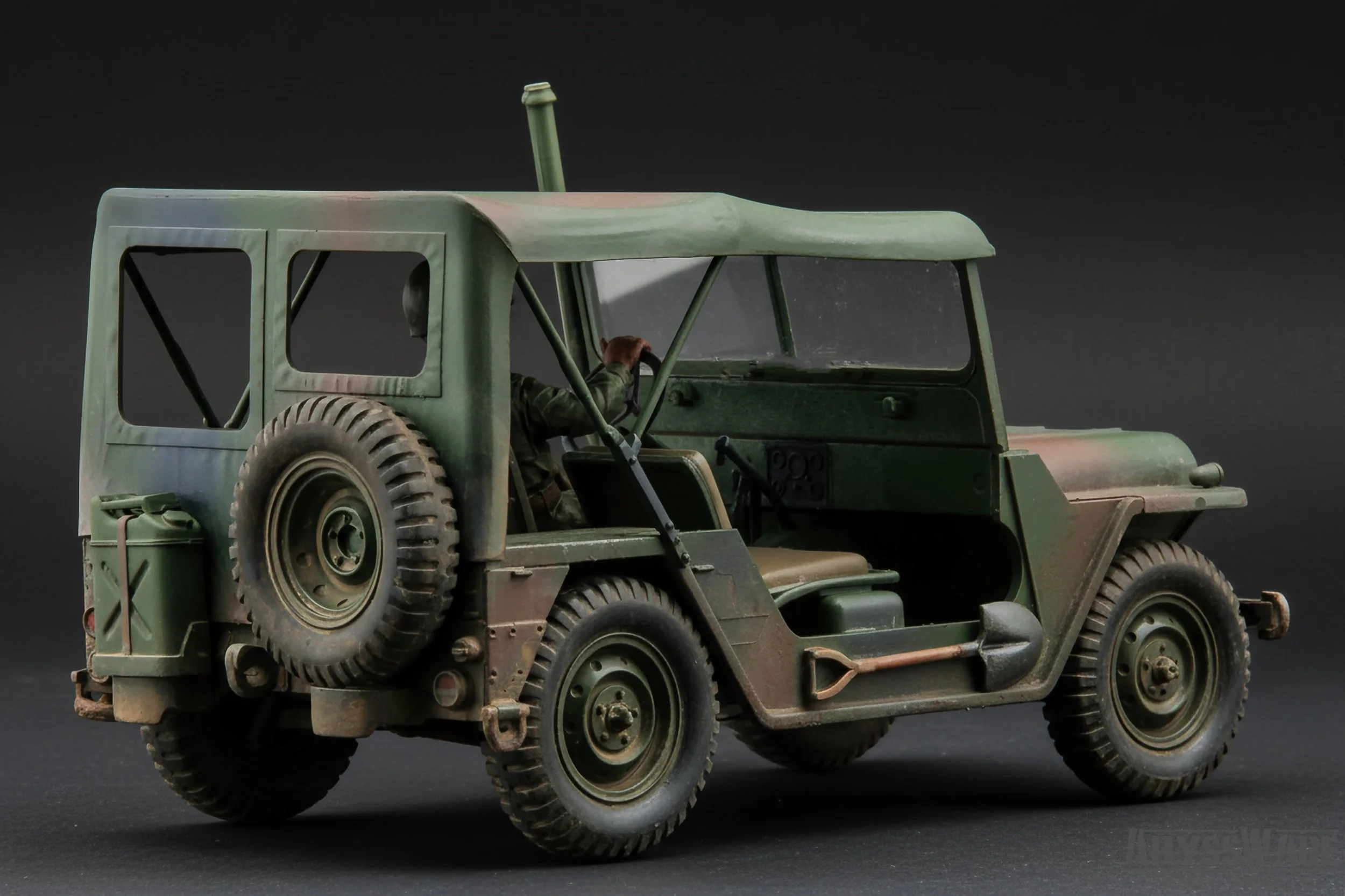 Model military vehicle with a spare tire and a soldier figure sitting in the driver's seat.