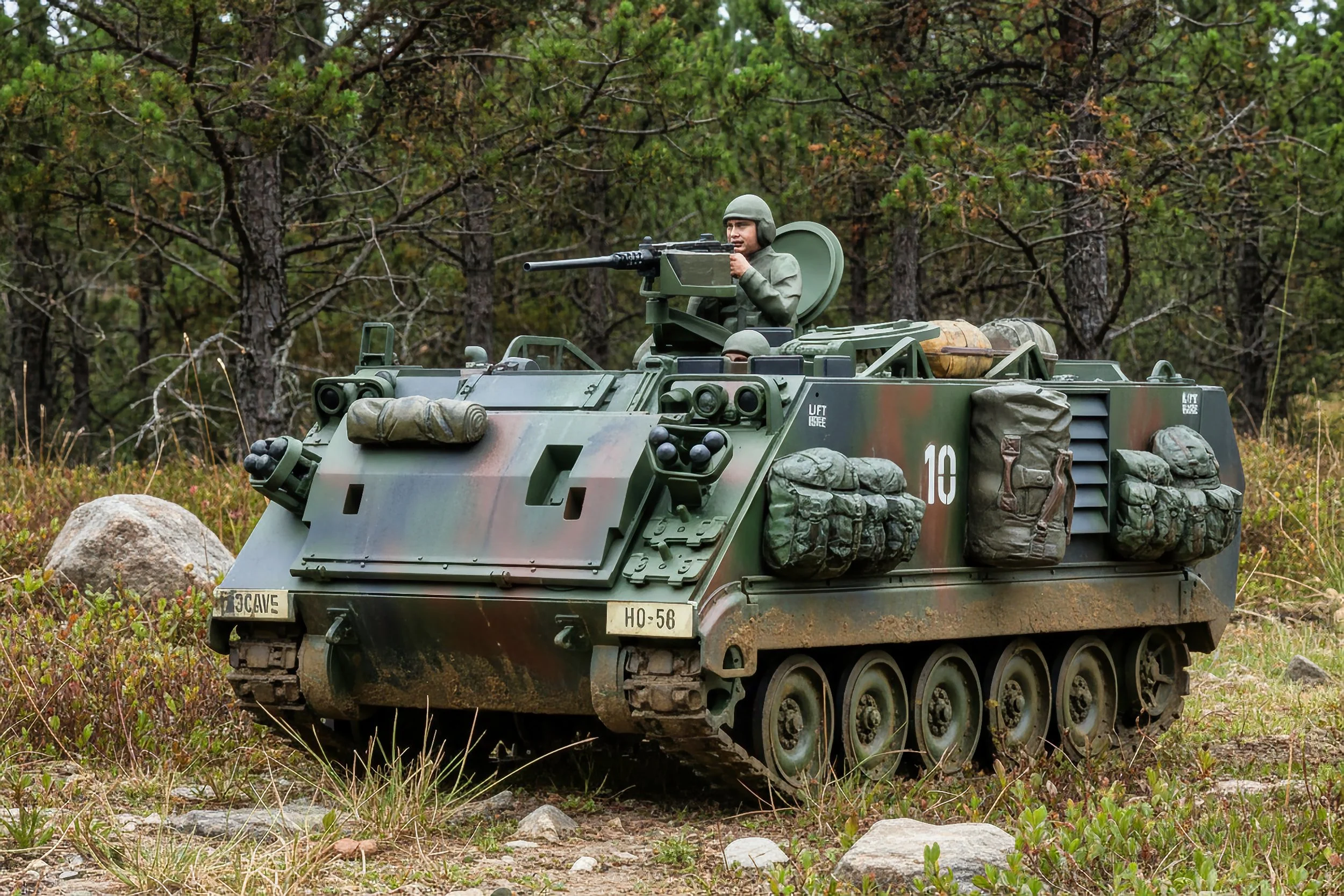 Military vehicle on grassy terrain with a soldier operating a mounted gun, surrounded by trees and rocks.