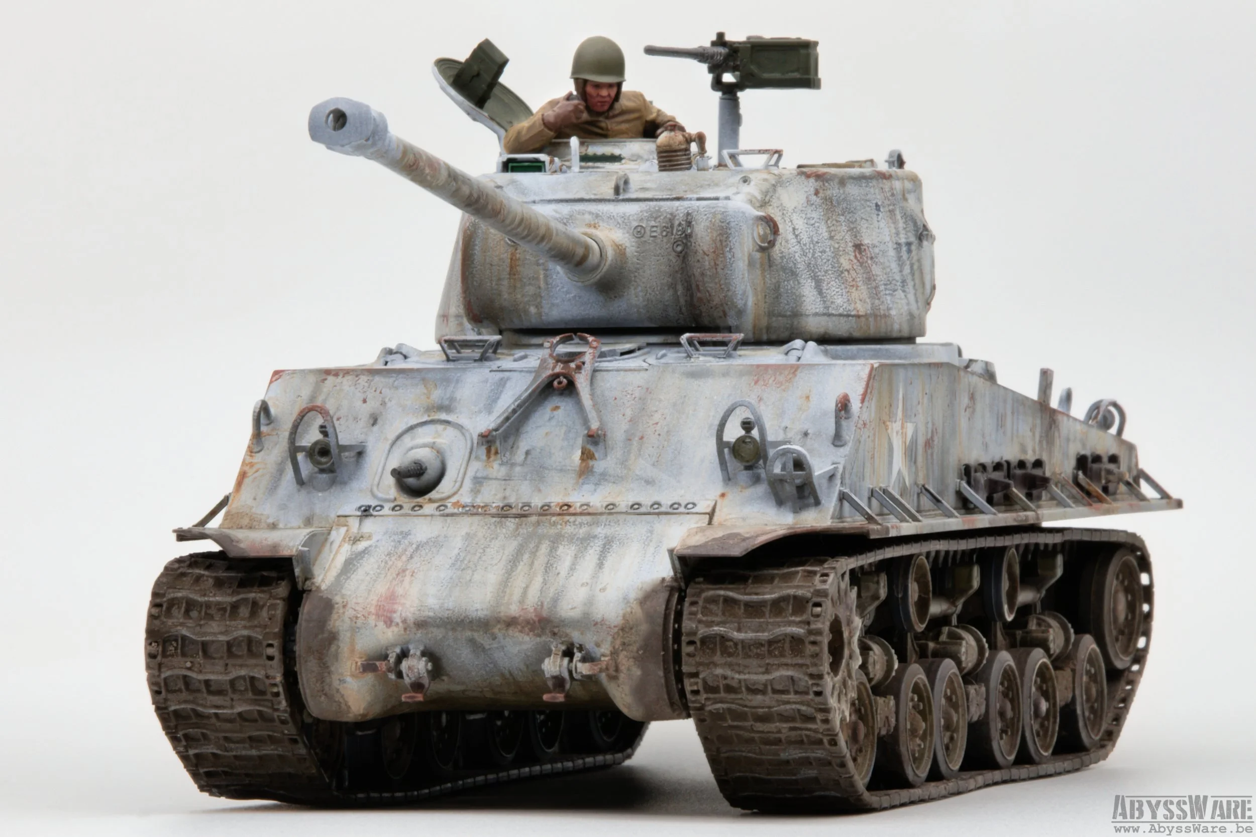 A miniature model of a military tank with a soldier figure in the turret. The tank has a weathered, rusty appearance and detailed tracks.