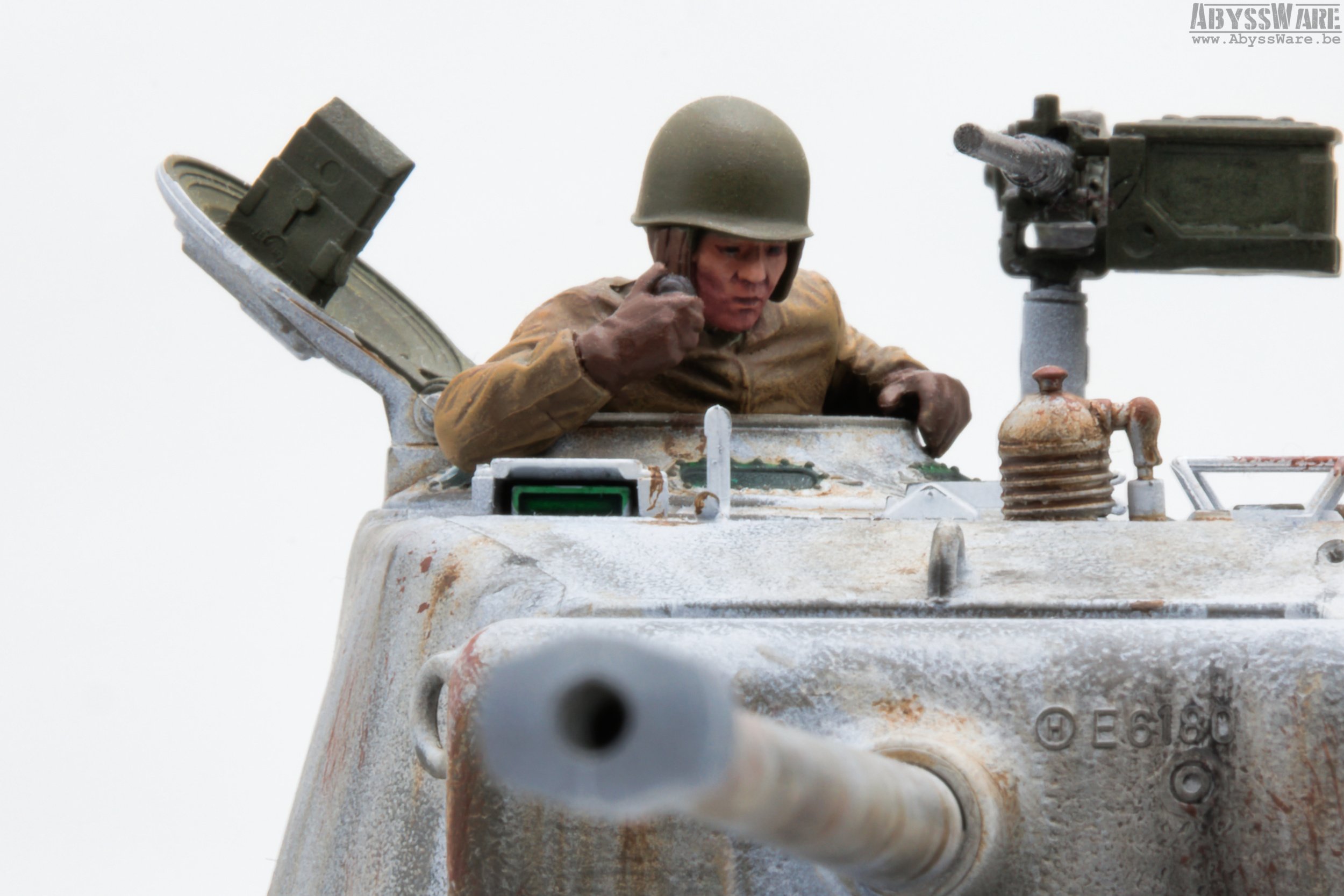 A miniature model of a soldier in military gear inside a tank, with the hatch open, and the soldier appearing to speak on a communication device.