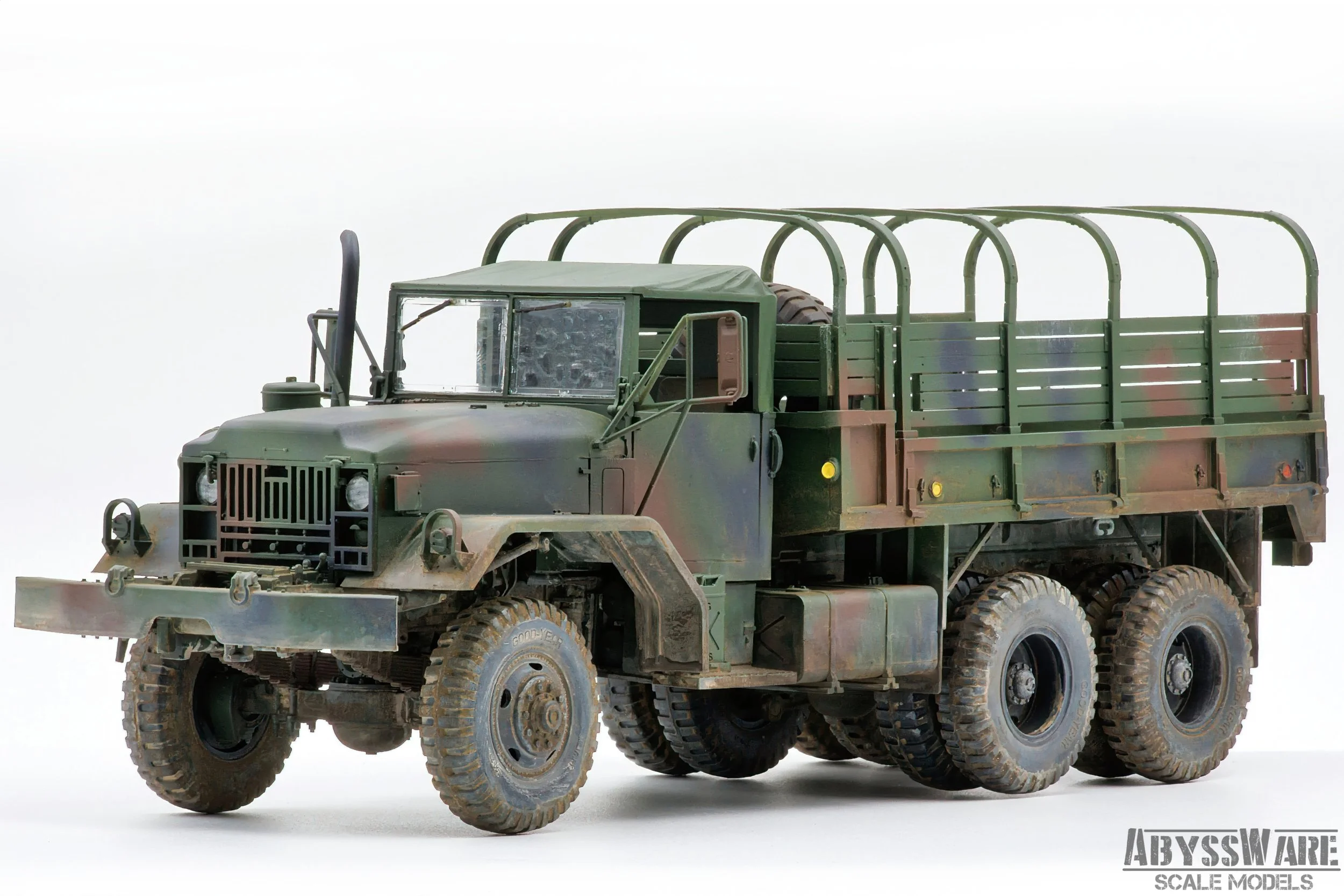 A detailed scale model of a military camouflage green cargo truck with six large tires, a flatbed with side rails, and an open cabin, displayed against a plain white background.