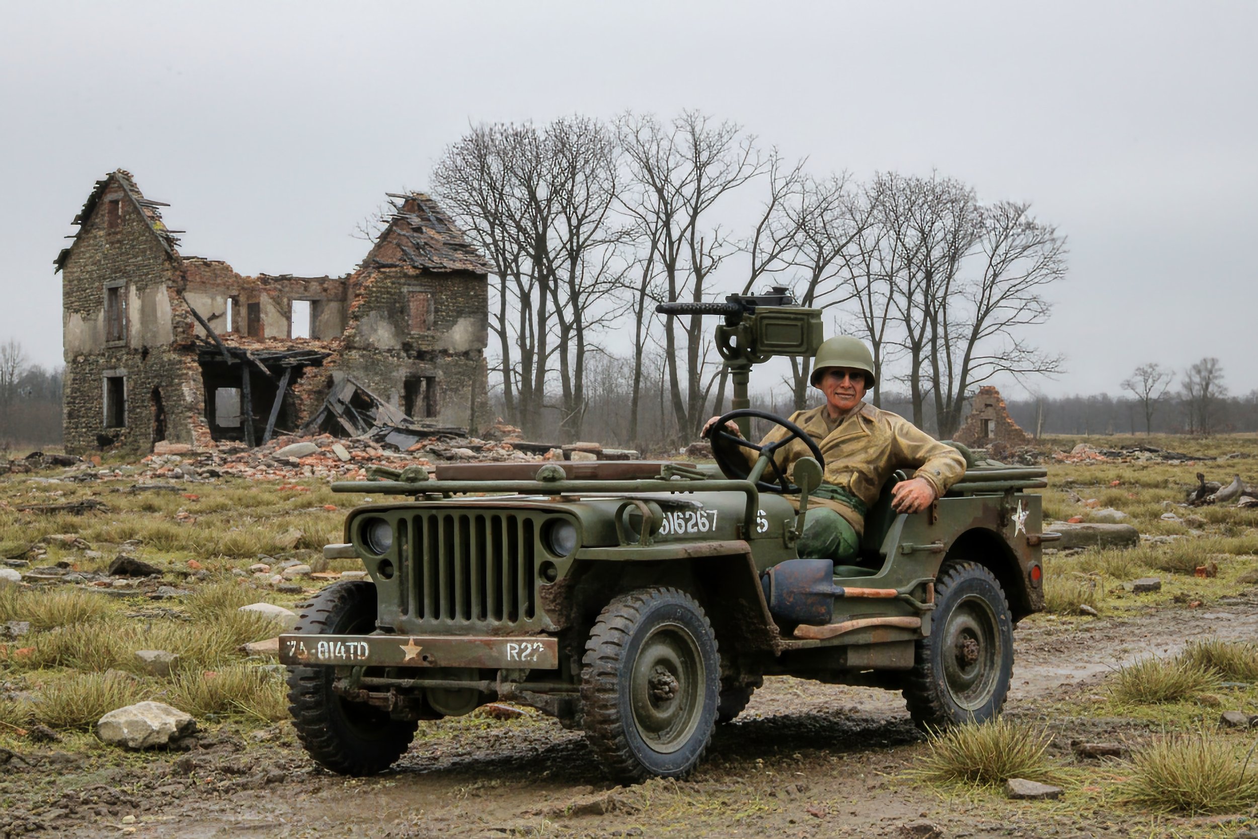 A person dressed in military uniform sitting in a vintage military jeep with a machine gun mounted on top, in front of a damaged building in a rural area.
