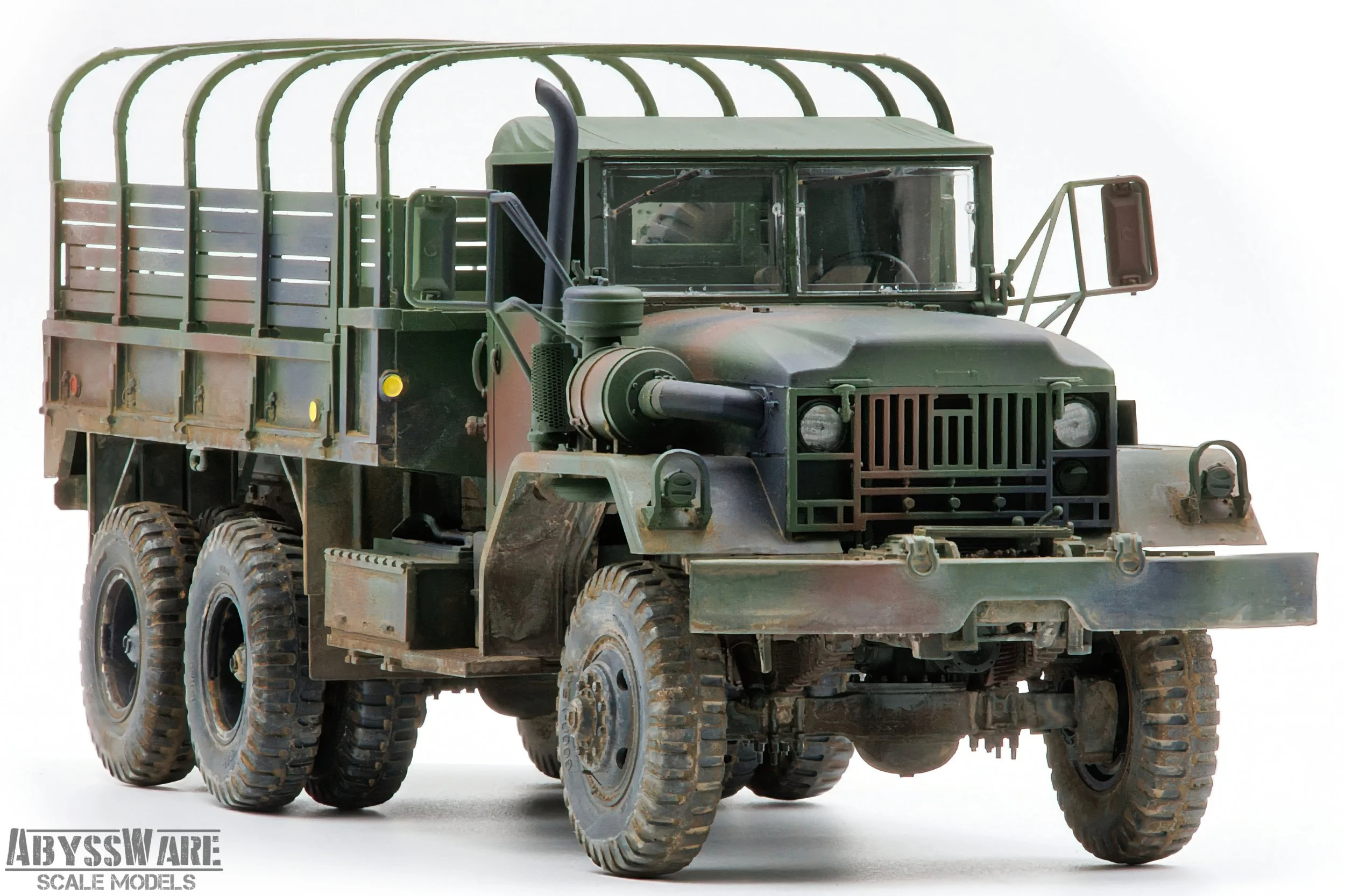 A detailed scale model of a military cargo truck with a camouflaged paint job, six wheels, a large front bumper, and a covered cargo bed with an arched green rack over it, set against a plain background.
