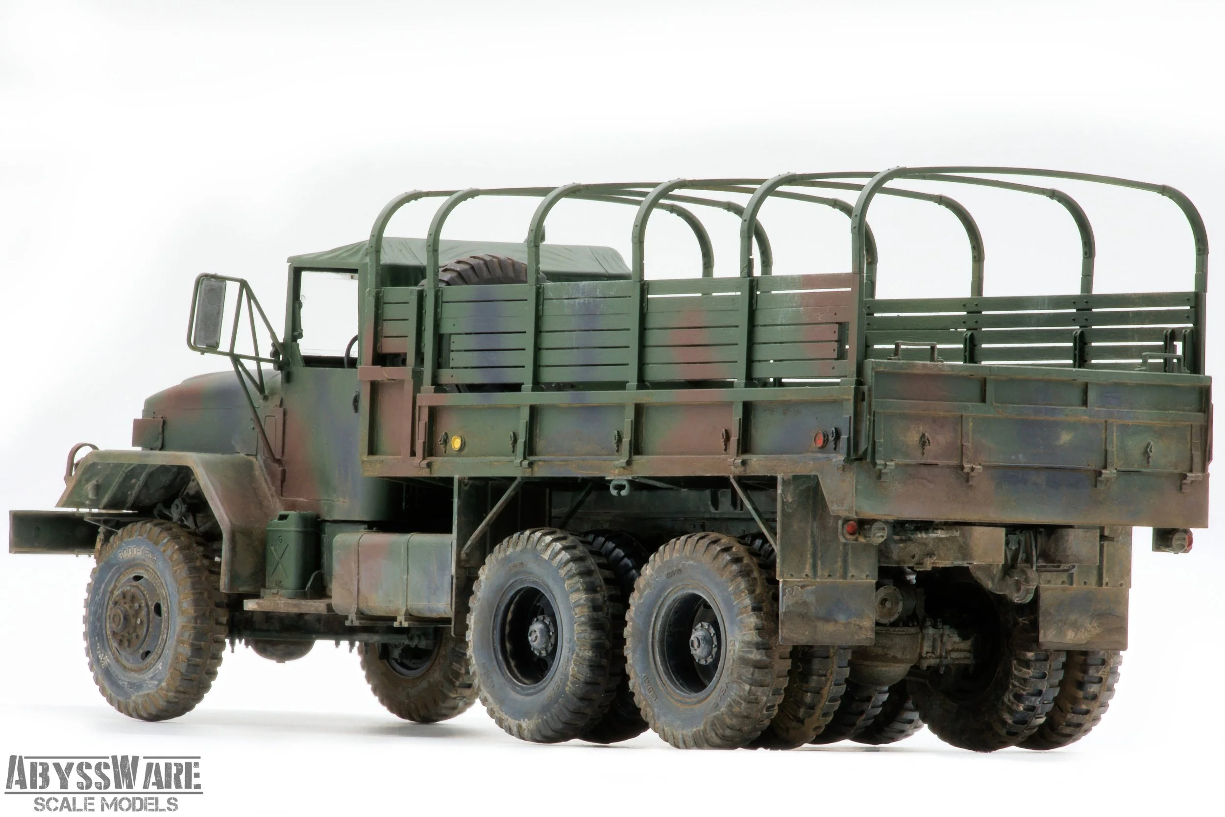 Scale model of a military cargo truck with a camouflage pattern, six large wheels, and a flatbed with railings.