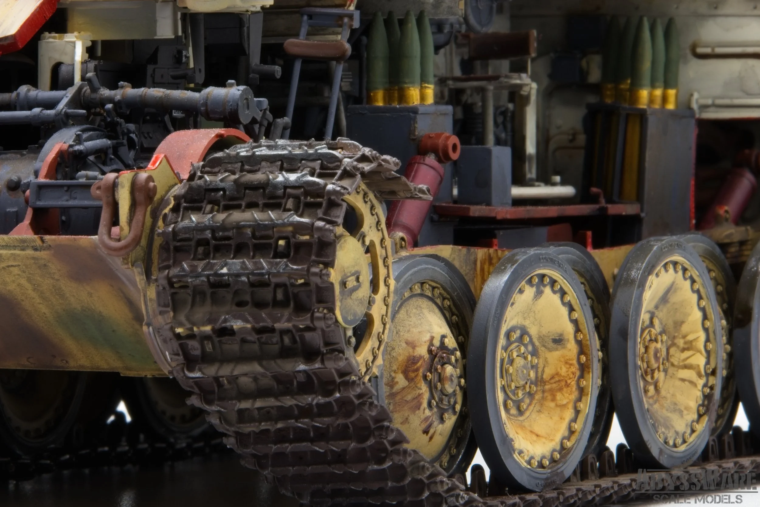 Close-up of a scale model tank's tracked wheels and suspension system, with detailed weathering and rust effects.