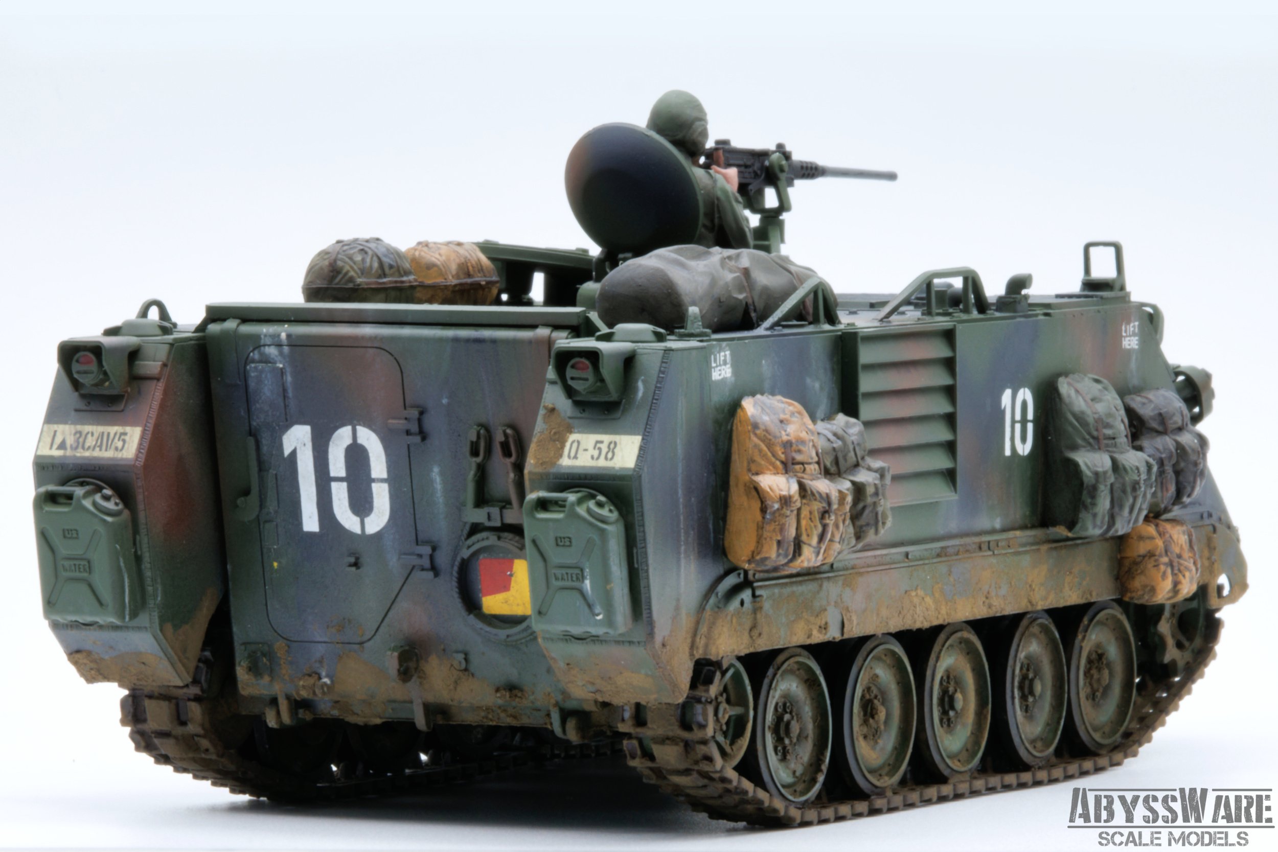 Model of a military armored tracked vehicle with a soldier figure on top aiming a rifle, painted in camouflage with various equipment attached.