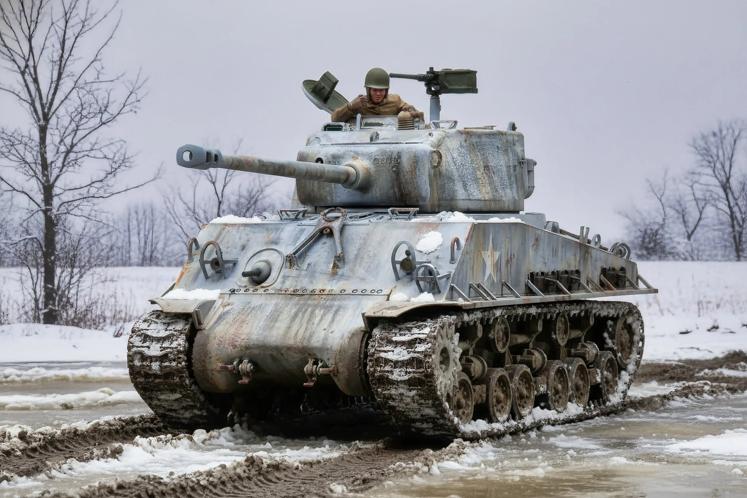 A military tank moving through snow with a soldier inside, trees in the background.