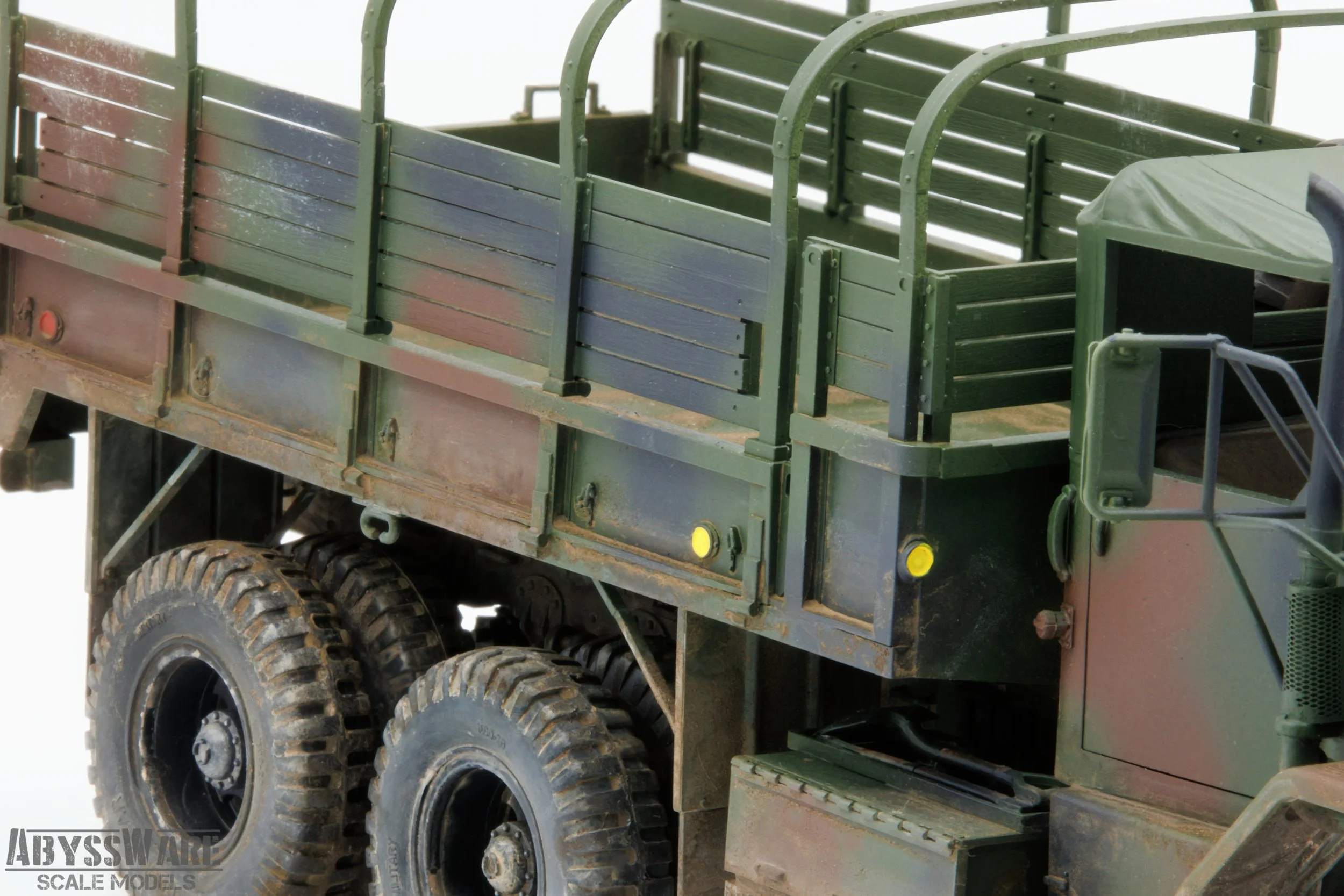 Close-up of a military green truck with a flatbed and wooden side panels, showing the rear tires and part of the cab.