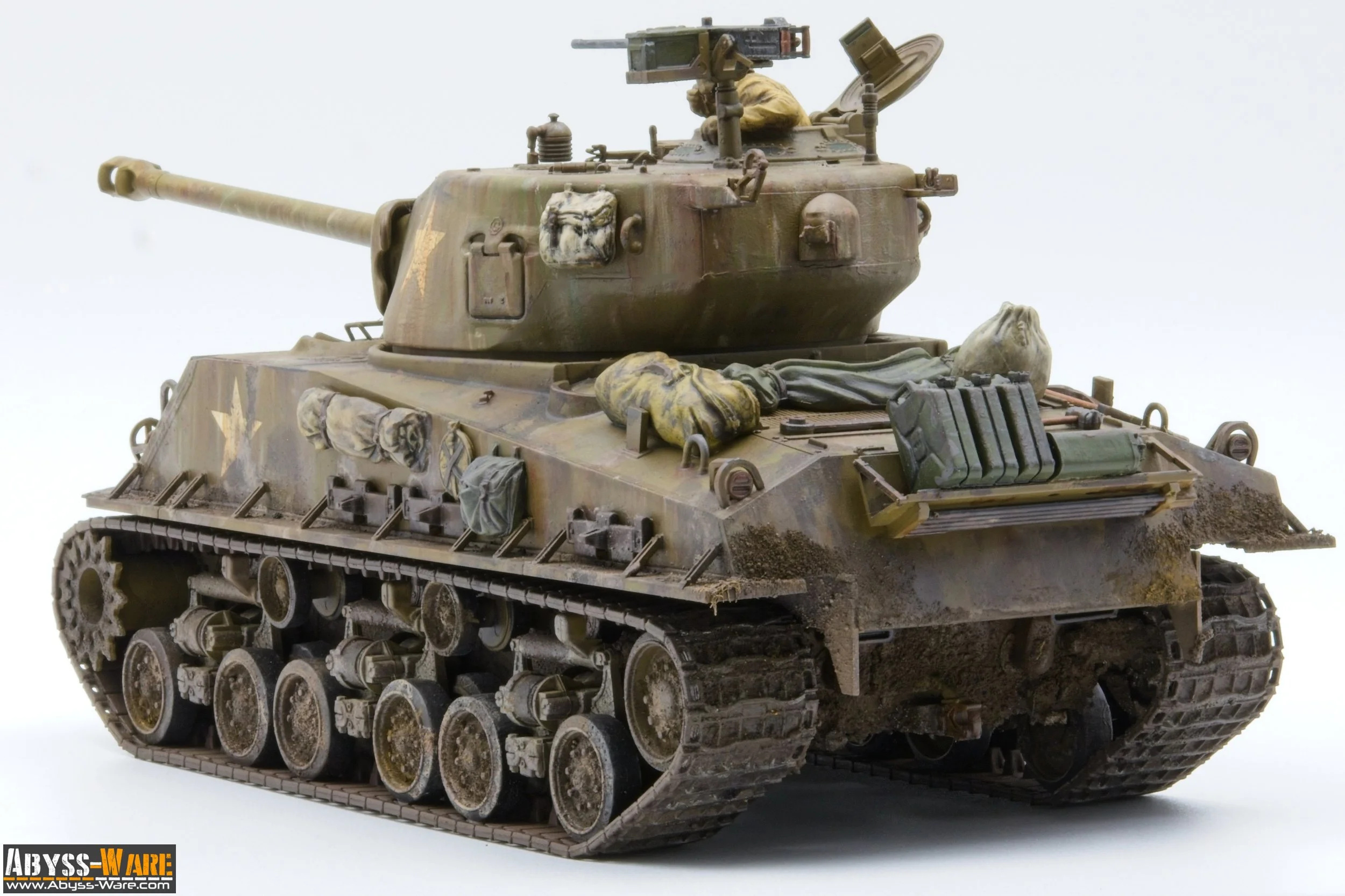 A detailed miniature model of a military tank with weathered camouflage paint, various supplies and gear on top, and a mounted machine gun on the turret, set against a plain white background.