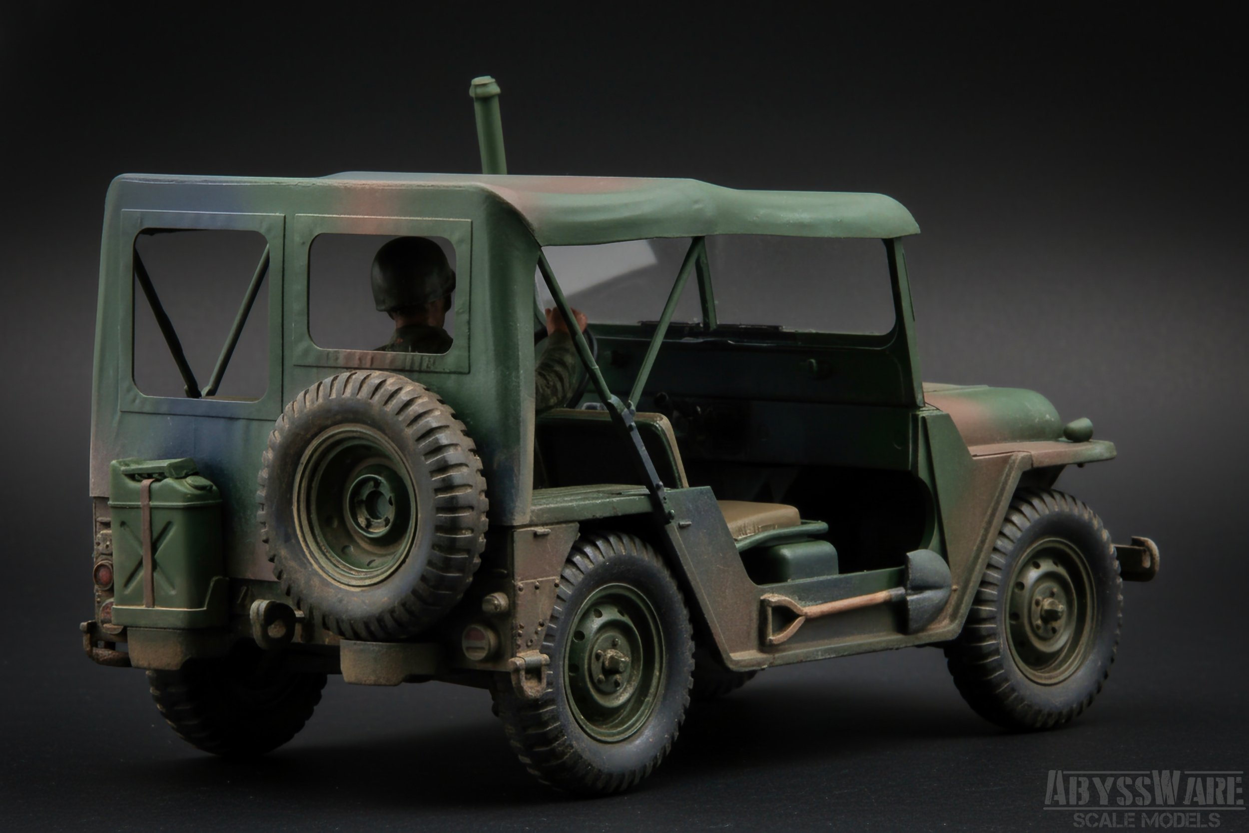 Military green scale model of a vintage off-road vehicle with a spare tire on the back and a soldier figure in the driver's seat, against a dark background.