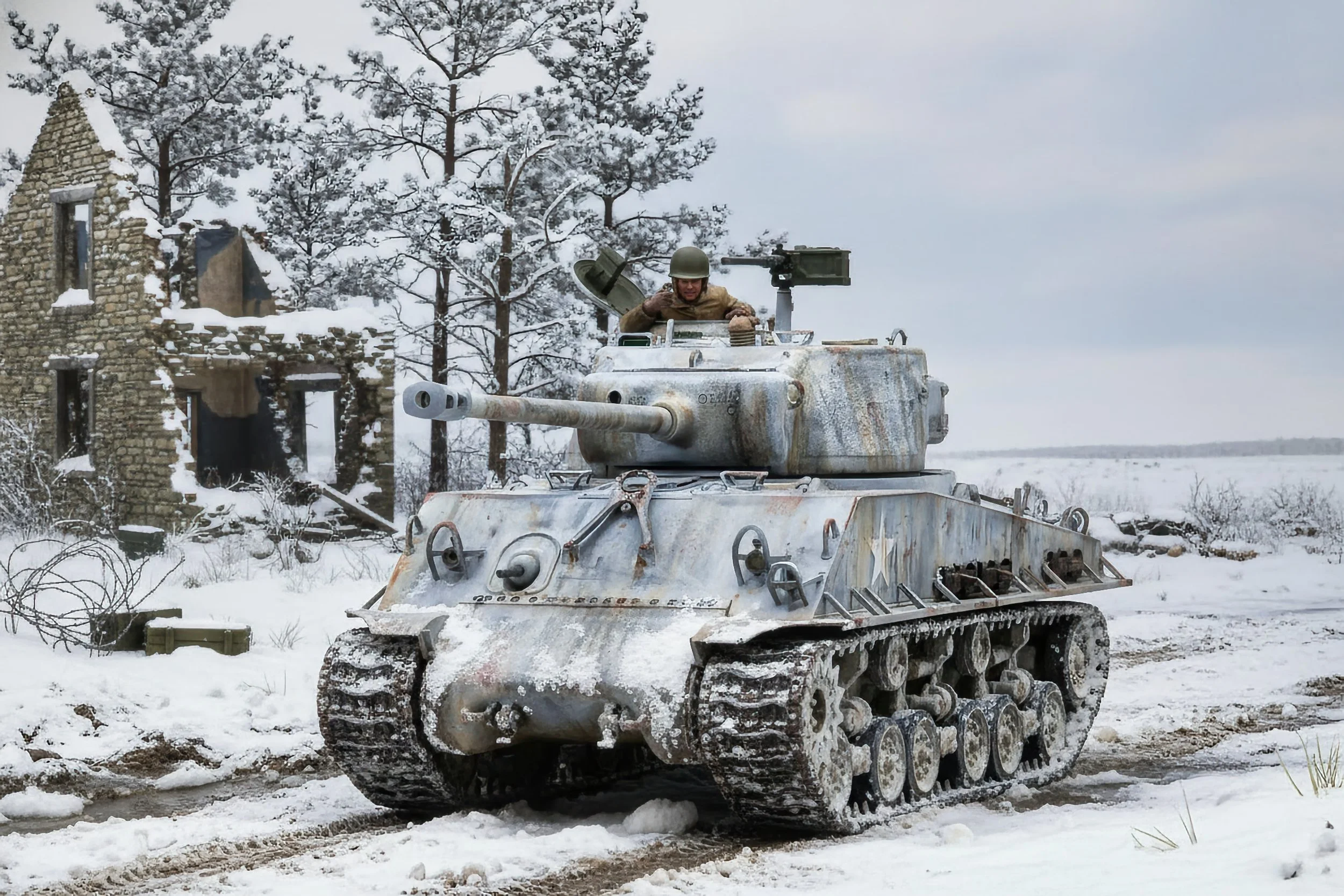 A soldier in a tan uniform and helmet inside a weathered, rust-colored tank driving through snow-covered ruins in a winter landscape with bare trees and a cloudy sky.