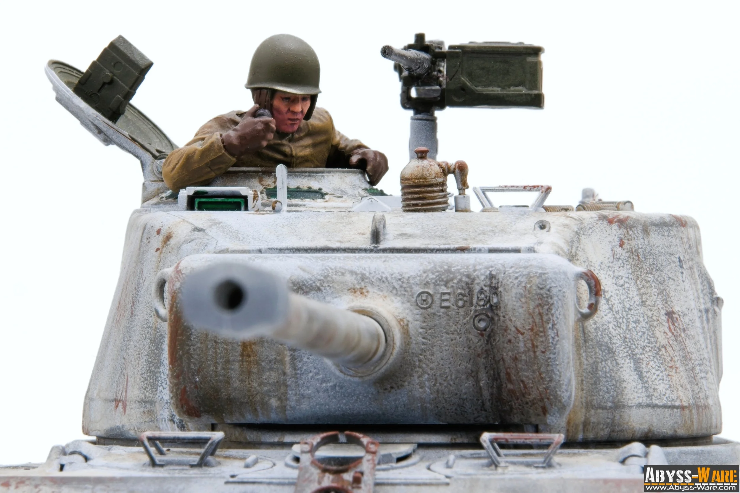 Model of a military tank with a soldier figurine inside. The tank has weathered, rusty details, and a person in a military helmet appears to be talking on a radio inside the open hatch.