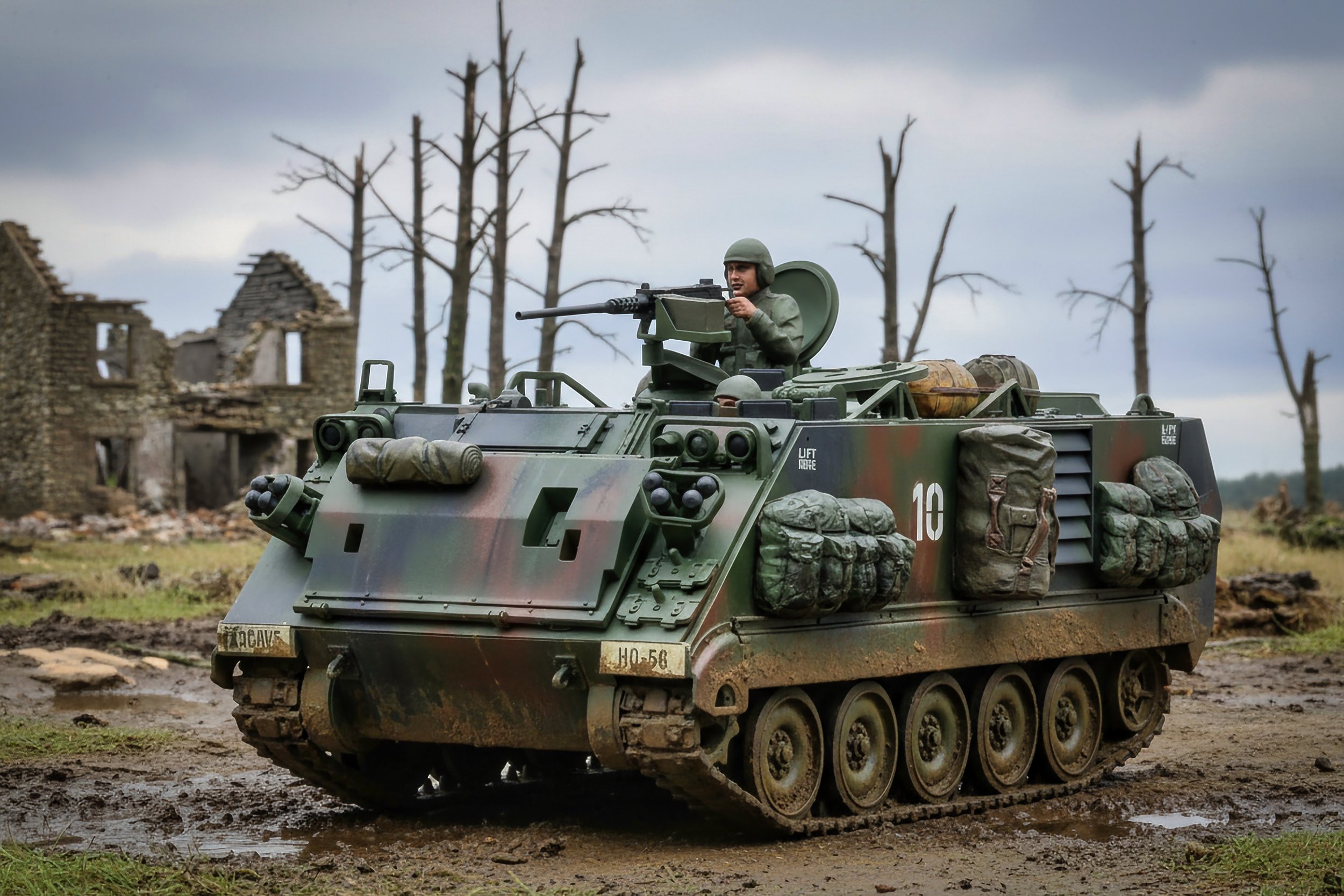 A military tank with a soldier in a helmet seems to be in a war-torn area with damaged buildings and leafless trees in the background.