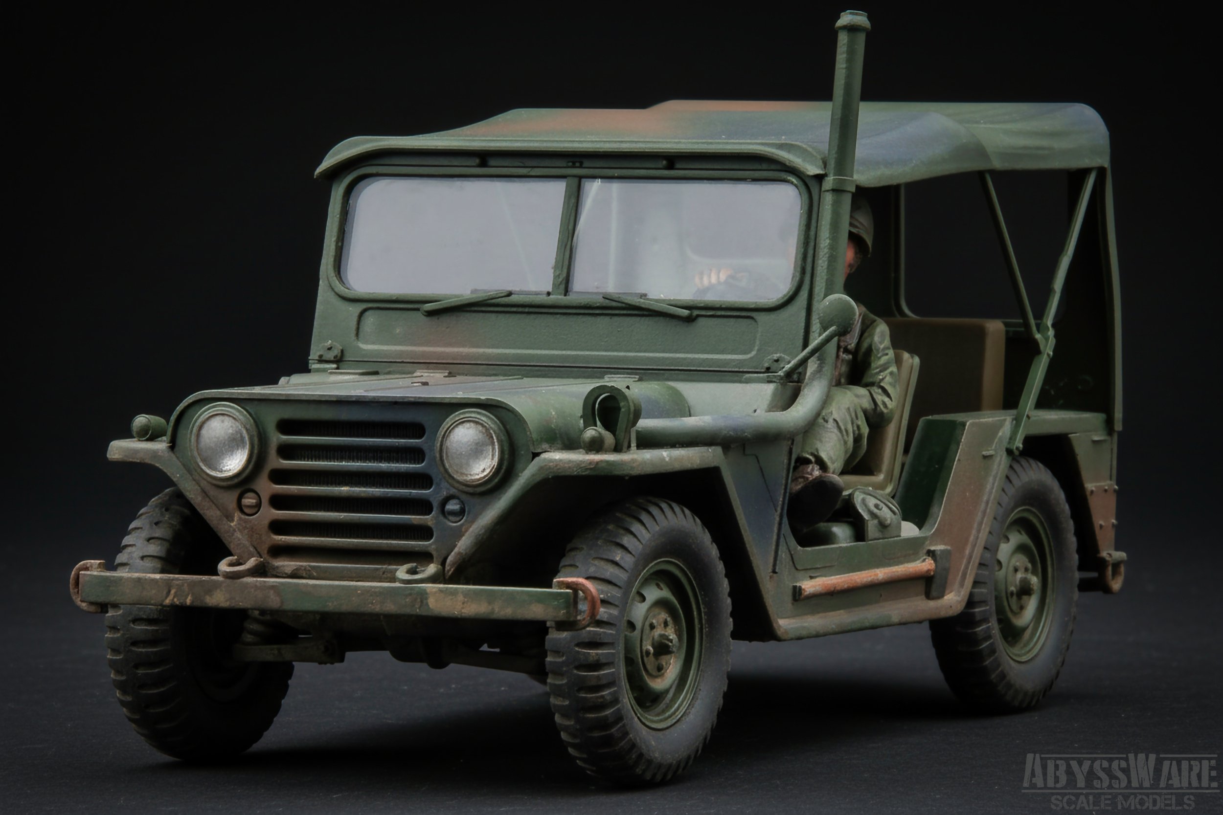A scale model of a military Jeep with a green, weathered finish and a seated driver figure in military attire.
