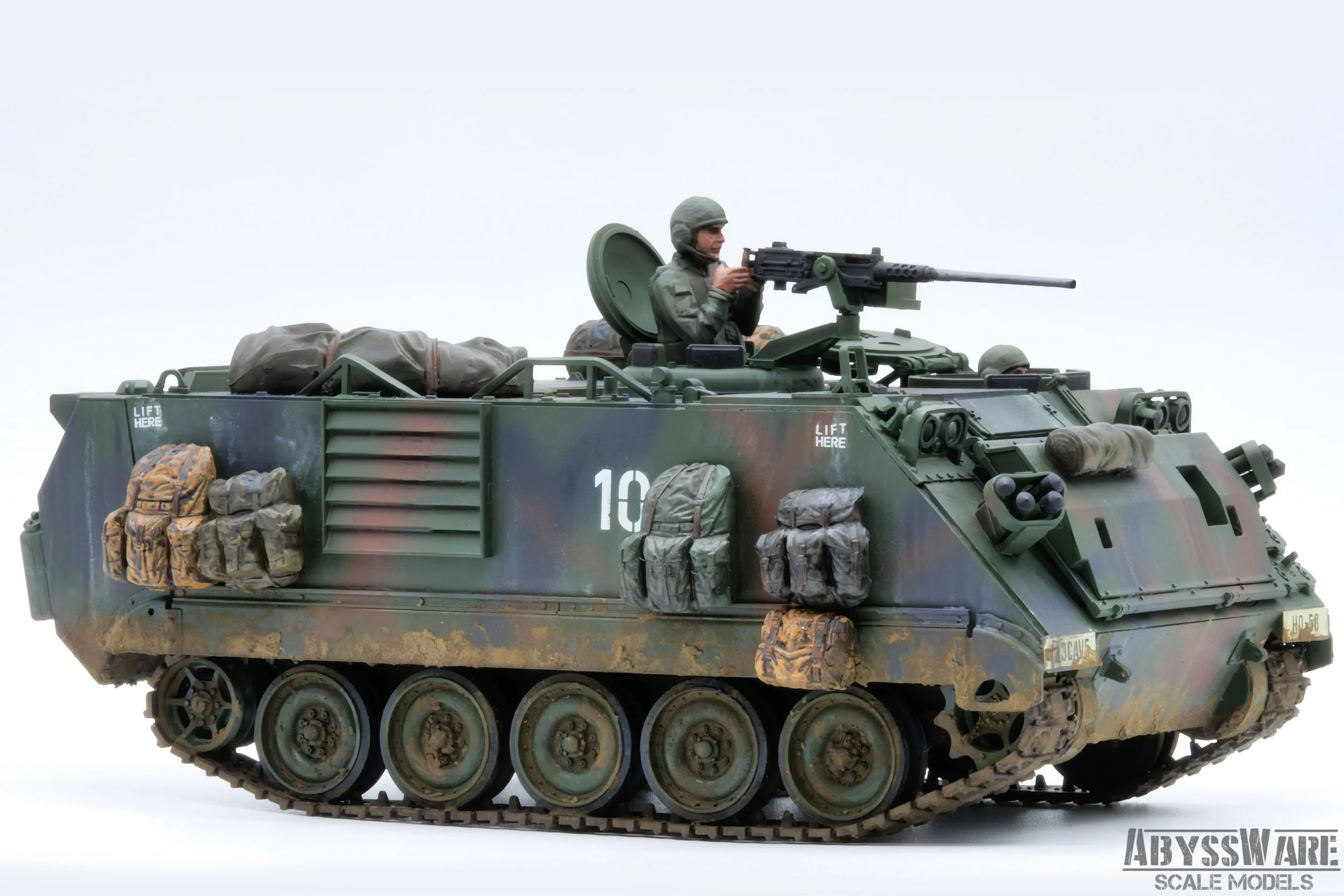 Model of a military armored vehicle with a mounted machine gun, carrying a soldier figurine, and equipped with various bags and gear on its sides, set against a plain white background.